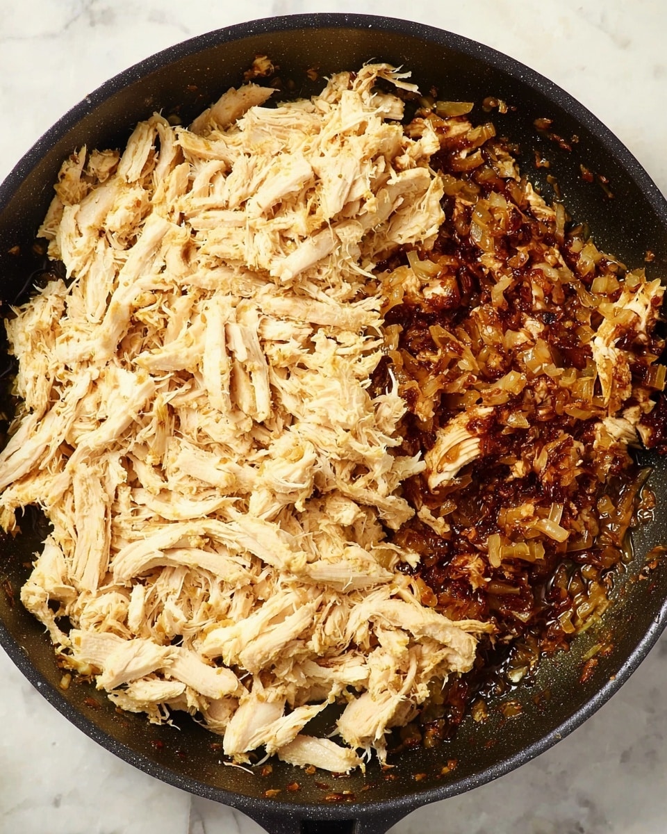 A black cooking pan filled with two main layers: on the left side, a large portion of shredded light beige cooked chicken with a soft, fibrous texture; on the right side, finely chopped and browned onions mixed with a slightly oily, dark reddish-brown cooked mixture, showing a caramelized and glossy look; the background surface is a white marbled texture. photo taken with an iphone --ar 4:5 --v 7