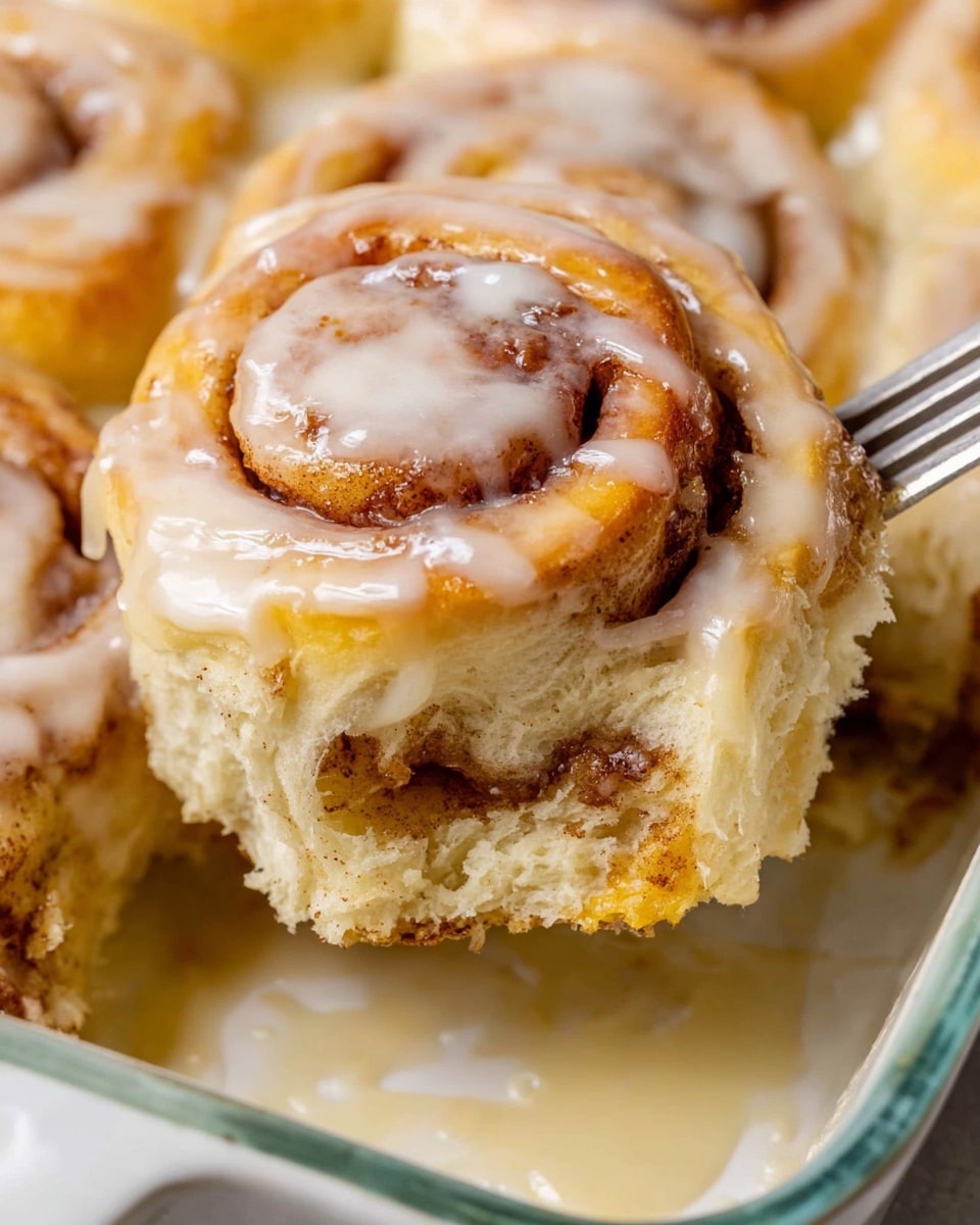 A close-up view of a soft cinnamon roll with visible three layers: a golden-brown swirled top coated in light white glaze, a middle layer of fluffy dough with darker cinnamon swirls, and a thicker, pale dough base. The cinnamon roll sits in a white marbled textured background with creamy glaze pooling around it in a white baking dish. A woman's hand is holding a fork that is gently lifting the cinnamon roll from the dish. The glaze shines in soft light, giving the whole image a fresh and warm feeling. photo taken with an iphone --ar 4:5 --v 7