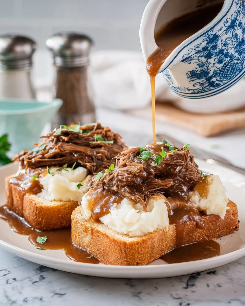 The image shows two thick slices of toasted bread as the bottom layer on a white plate. On top of each slice is a generous layer of smooth, creamy mashed potatoes that look fluffy and white. Above the potatoes is a pile of shredded brown meat covered in a rich, thick brown gravy being poured from a blue and white patterned gravy boat. The meat is garnished with small green herb pieces, adding color contrast. The plate sits on a white marbled surface, and a blurred salt and pepper shaker set is visible in the background. Photo taken with an iphone --ar 4:5 --v 7