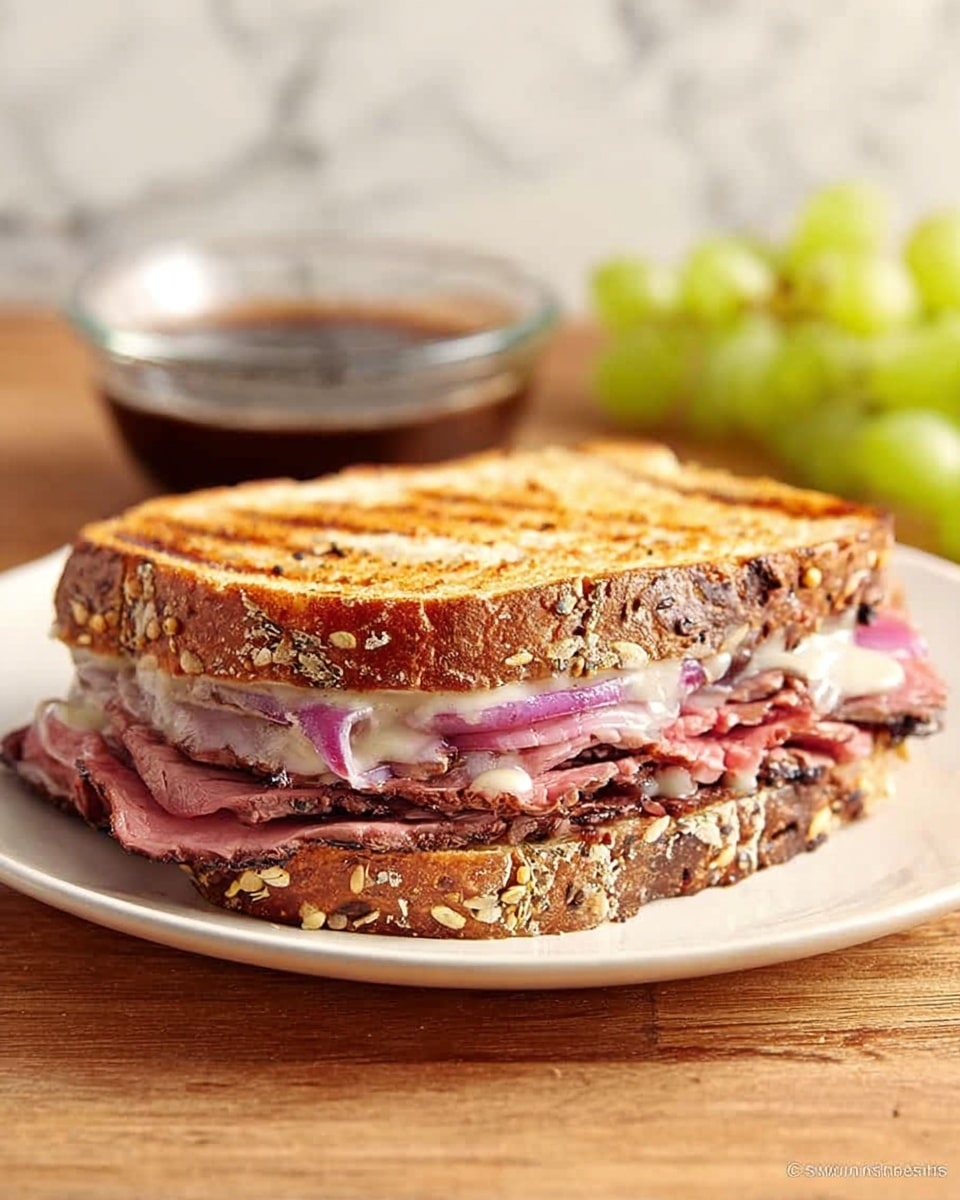 The image shows a grilled sandwich on a white plate placed on a wooden surface with a white marbled background. The sandwich has two toasted slices of multigrain bread with visible seeds on the crust. Inside, there is a layer of thinly sliced pink roast meat, likely roast beef, topped with a creamy sauce, along with thin slices of red onion visible just beneath the top bread layer. In the background, there are green grapes and a small clear bowl of dark sauce, slightly blurred to keep focus on the sandwich. Photo taken with an iphone --ar 4:5 --v 7