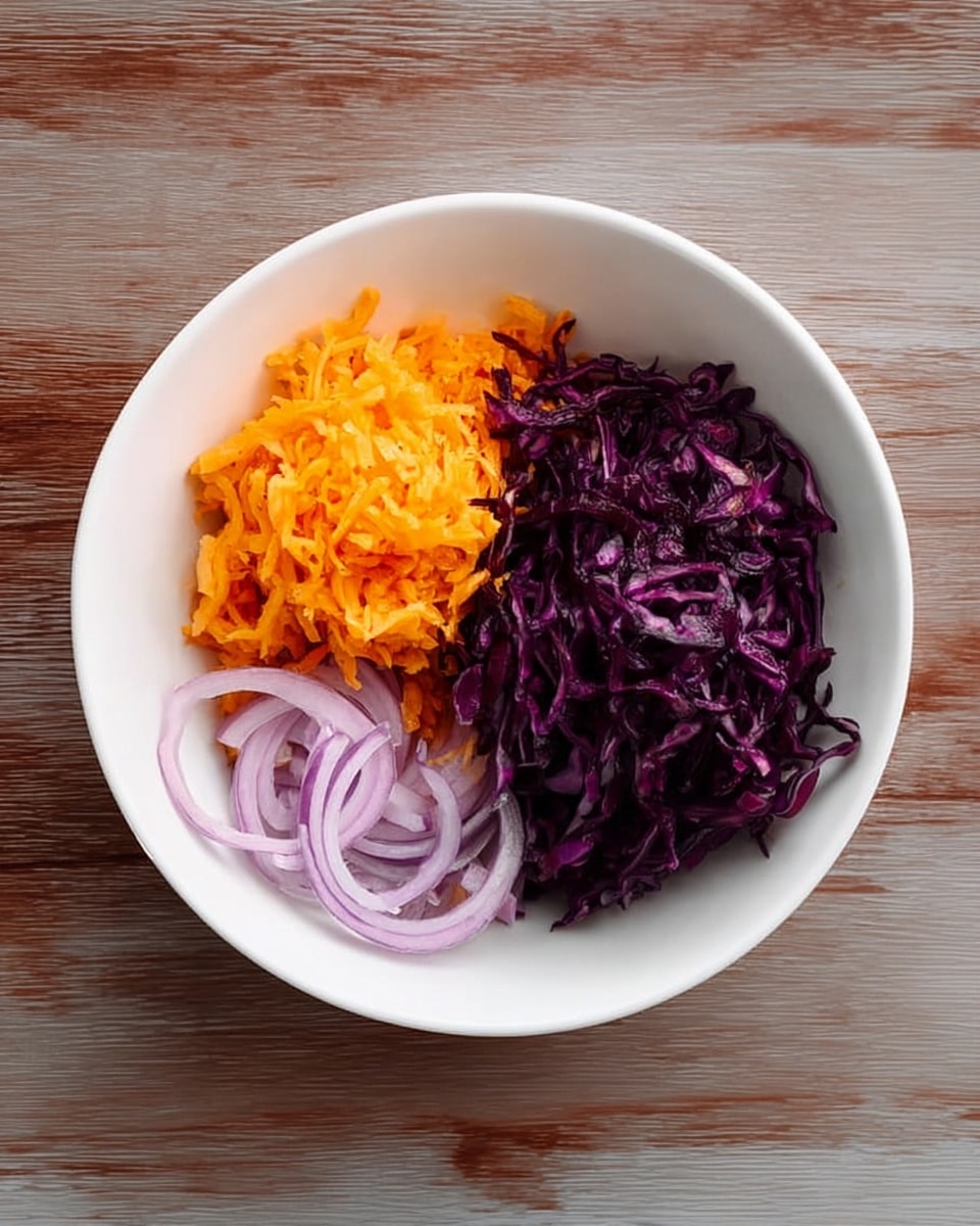 A white bowl on a white marbled surface holds three layers of vegetables. On the right, there is a large pile of dark purple shredded cabbage with thin, curly pieces. On the left, below the cabbage, there is a small pile of light purple, thinly sliced onions with curved rings. Above the onions, there is a rounded mound of bright orange shredded carrot. The bowl and vegetables are shown from above with clear, sharp details. Photo taken with an iphone --ar 4:5 --v 7