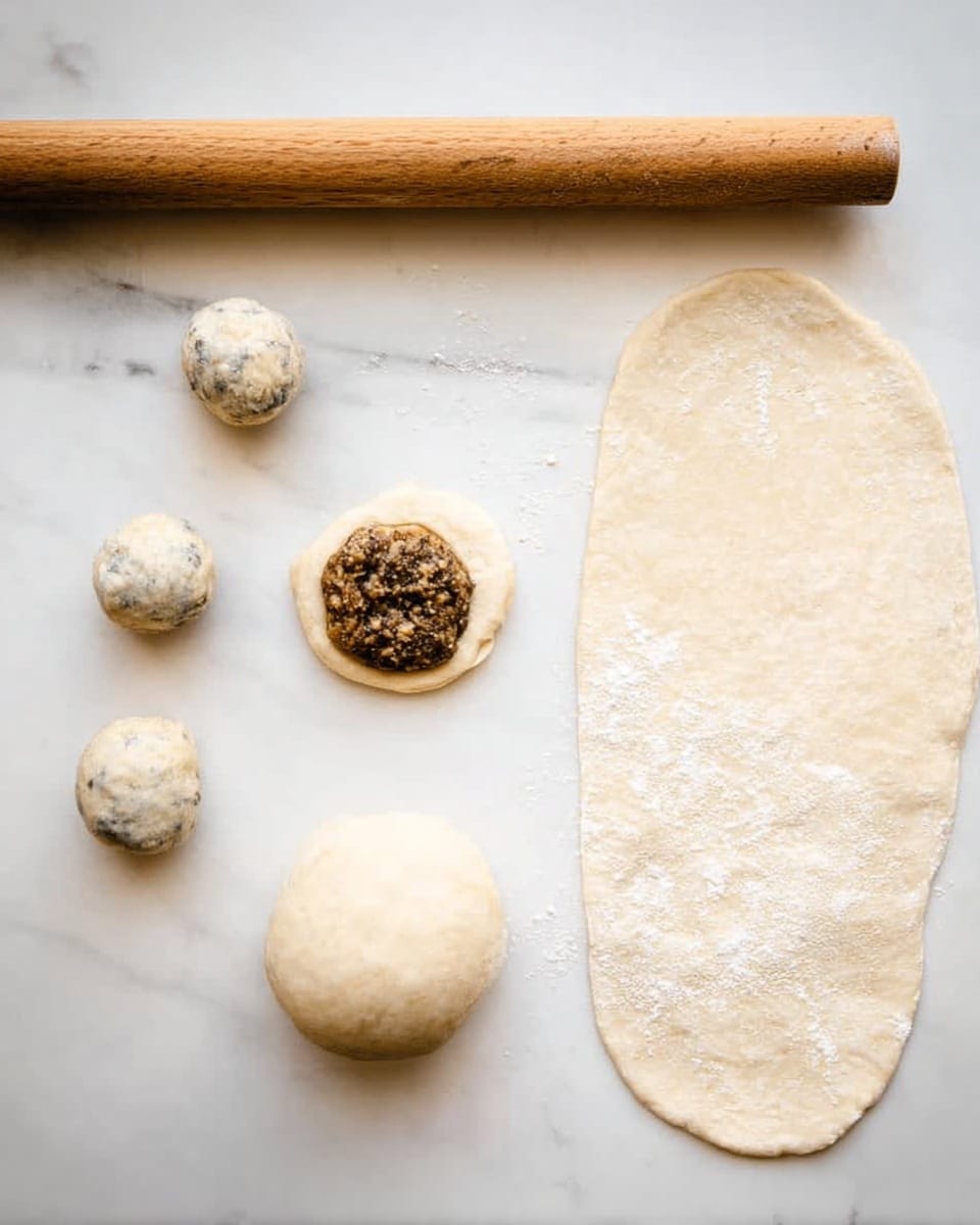 The image shows a white marbled surface with five pieces of dough in different stages. On the left, there are three small rough dough balls placed vertically. At the center, a small dough ball is flattened and topped with a dark, textured filling. To the right of it, there is a smooth round dough ball. Further right, a large flattened oval dough piece dusted with flour is placed horizontally. At the top of the image, there is a wooden rolling pin resting horizontally. The overall colors include pale dough with some brown filling and light dusting of flour. photo taken with an iphone --ar 4:5 --v 7