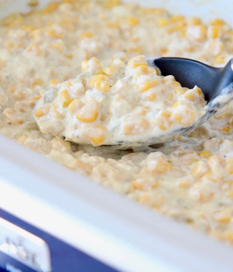A close-up image of creamy corn casserole in a white baking dish placed on a white marbled surface. The dish shows one thick layer of yellow corn mixed in a pale creamy, textured sauce with visible black pepper specks. A black spoon is scooping a portion of the mixture from the dish, showing the thick and rich texture of the creamy corn inside. The edges of the baking dish are visible in the frame, adding contrast to the pale creamy yellow corn mixture. photo taken with an iphone --ar 4:5 --v 7