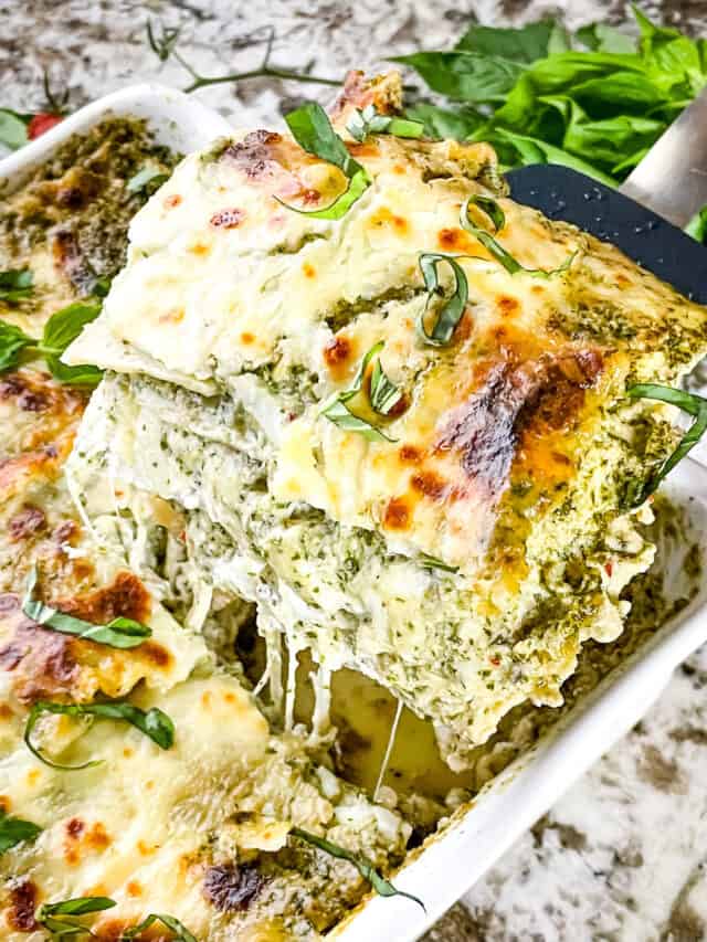 Lasagna al Pesto Recipe 5 A white dish filled with a tall, multi-layered lasagna showing about five visible layers of creamy pesto sauce, white cheese, and pasta sheets. The top layer is golden with melted cheese and browned spots, sprinkled with thin green basil strips. The layers have a smooth texture with some cheese stretching as a slice is lifted by a black spatula, and the background is a white marbled surface. Photo taken with an iphone --ar 4:5 --v 7