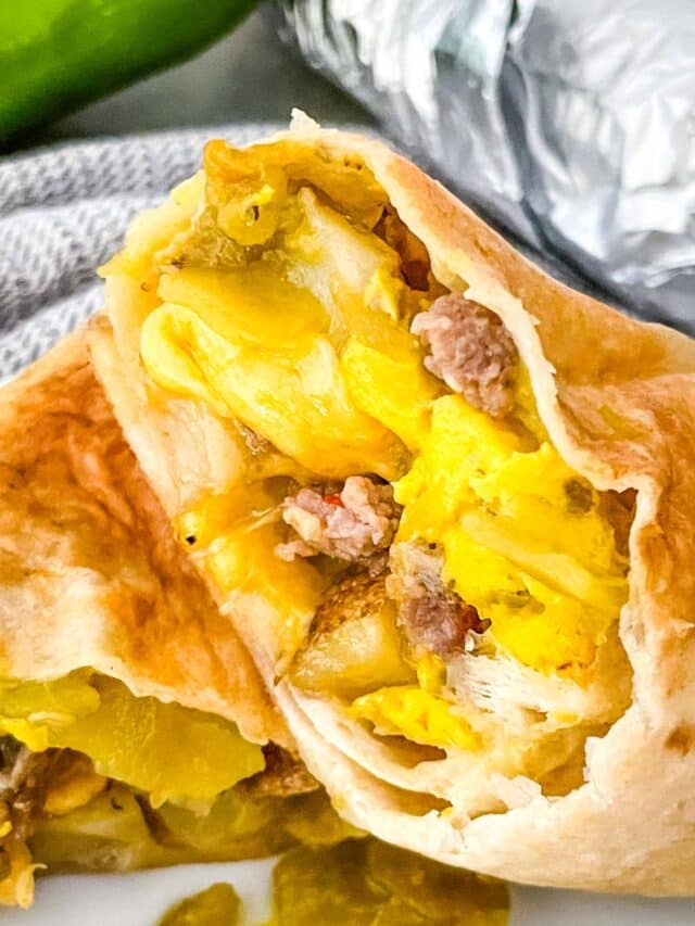 The image shows a close-up of a breakfast burrito cut open to reveal three thick layers: the outer layer is a light golden-brown, soft tortilla wrap with slight crisp spots; the middle layer is scrambled eggs in bright yellow with soft texture; inside the eggs are small pieces of browned sausage meat, adding a crumbly texture; there are also bits of cooked potatoes with a pale yellow color and slightly crispy edges, mixed with some green chili pieces adding color contrast; the burrito sits on a white plate with a white marbled background visible behind it. Photo taken with an iphone --ar 4:5 --v 7