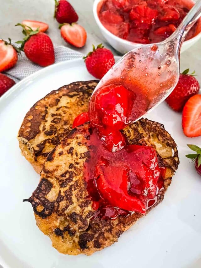 The image shows two thick golden-brown pancakes stacked on a white plate, with a shiny, bright red strawberry sauce spooned over the top pancake. The strawberry sauce has large chunks of strawberries and looks glossy and juicy. Around the plate are several whole and sliced strawberries, adding fresh red and green colors. Behind the plate, a matching white bowl filled with more strawberry sauce is partly visible. The whole setup is on a white marble surface, and a woman's hand holding the spoon is gently placing the sauce on the pancakes. photo taken with an iphone --ar 4:5 --v 7
