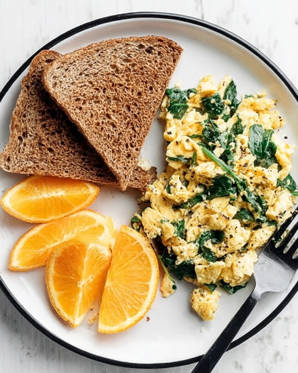A white plate with a thin black rim holds three food items arranged in three sections: on the top left, two toasted brown whole grain triangular slices are stacked slightly overlapping; on the bottom left, three bright orange, juicy orange wedges are placed side by side; on the right, a serving of scrambled eggs mixed with wilted green spinach rests, with the eggs showing a soft, slightly creamy texture and small black pepper bits visible; a black fork is partially tucked under the eggs on the bottom right corner of the plate; the whole scene is set on a white marbled surface. photo taken with an iphone --ar 4:5 --v 7