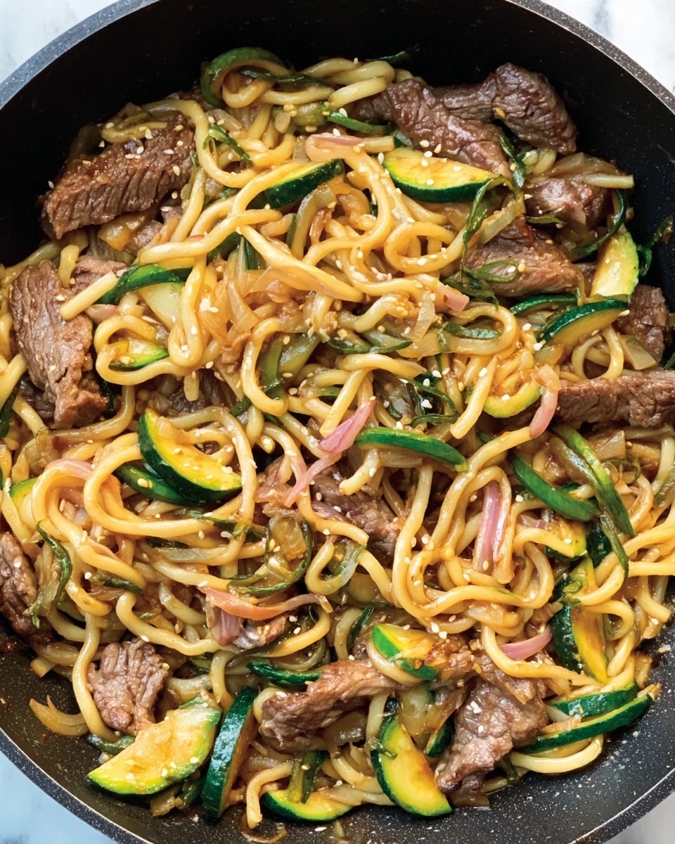 A close-up view of a dark cooking pan filled with a stir-fry dish containing thick light yellow noodles spread evenly throughout, mixed with cooked brown strips of beef scattered across the pan. Sliced green zucchini pieces with tender textures and thin pink slices of shallots are mixed in, creating a colorful contrast. Small white sesame seeds are sprinkled throughout the dish, adding texture against the glossy, slightly oily look of the ingredients. The pan sits on a white marbled surface. photo taken with an iphone --ar 4:5 --v 7