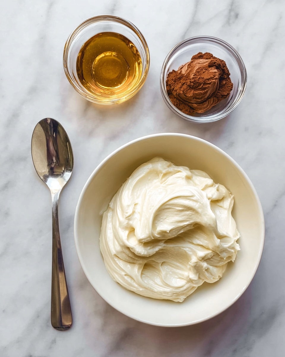 A close-up shot of a creamy white substance in a large white bowl with a smooth texture and slight peaks, surrounded by three small clear glass bowls—one with a glossy dark golden liquid, one with a thick brown nutty paste, and one with a fine cocoa or chocolate powder. Near the bowls is a large shiny silver spoon resting on a white marbled surface, all arranged neatly in an overhead view. photo taken with an iphone --ar 4:5 --v 7