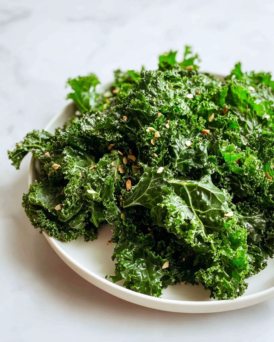 A white plate holds a pile of dark green, curly kale leaves. The kale is fresh and crisp, with each leaf showing detailed ruffled edges and visible veins. Scattered on top are small bits of light brown and cream-colored seeds or flakes, adding contrast and texture. The plate sits on a white marbled surface with soft natural light shining from one side, enhancing the fresh and healthy look of the kale. photo taken with an iphone --ar 4:5 --v 7