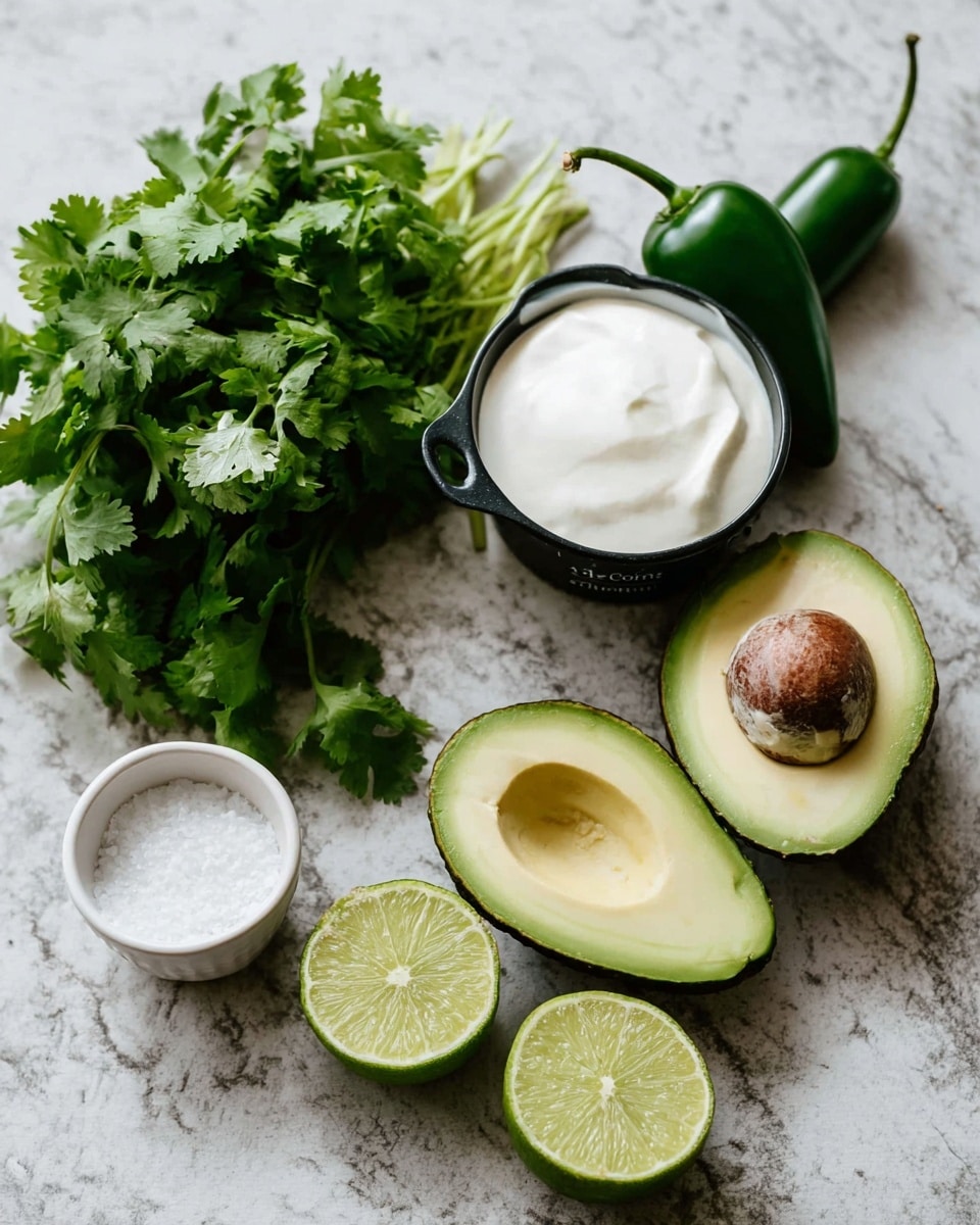 The image shows fresh ingredients laid out on a white marbled surface: a bunch of bright green cilantro leaves with some stems, a shiny dark green jalapeño pepper, a black measuring cup filled with smooth white sour cream on the top right, a halved avocado with a large brown seed inside and its other half showing the creamy light green flesh, two halves of a light green lime with visible juicy segments, and a small white bowl filled with white salt. photo taken with an iphone --ar 4:5 --v 7