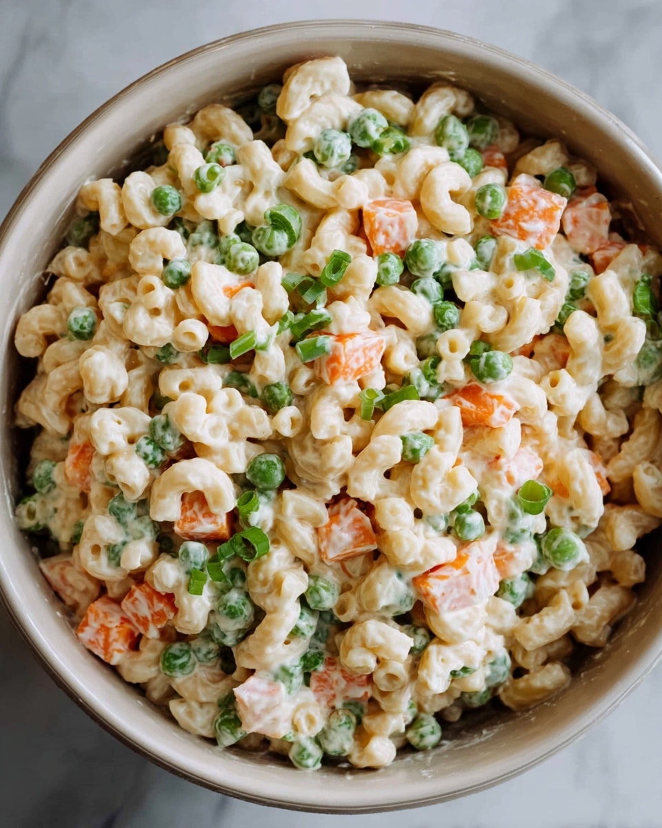 The image shows a close-up of a creamy macaroni salad in a round white bowl. The dish has three visible layers: the main layer of small elbow macaroni pasta coated in a thick, smooth, light cream sauce; mixed evenly with bright orange small carrot cubes and green peas; and topped with chopped green onions sprinkled throughout, adding a fresh touch. The bowl is placed on a white marbled surface, and the textures of the pasta and vegetables are clear, with the creamy layer giving a soft shine. photo taken with an iphone --ar 4:5 --v 7
