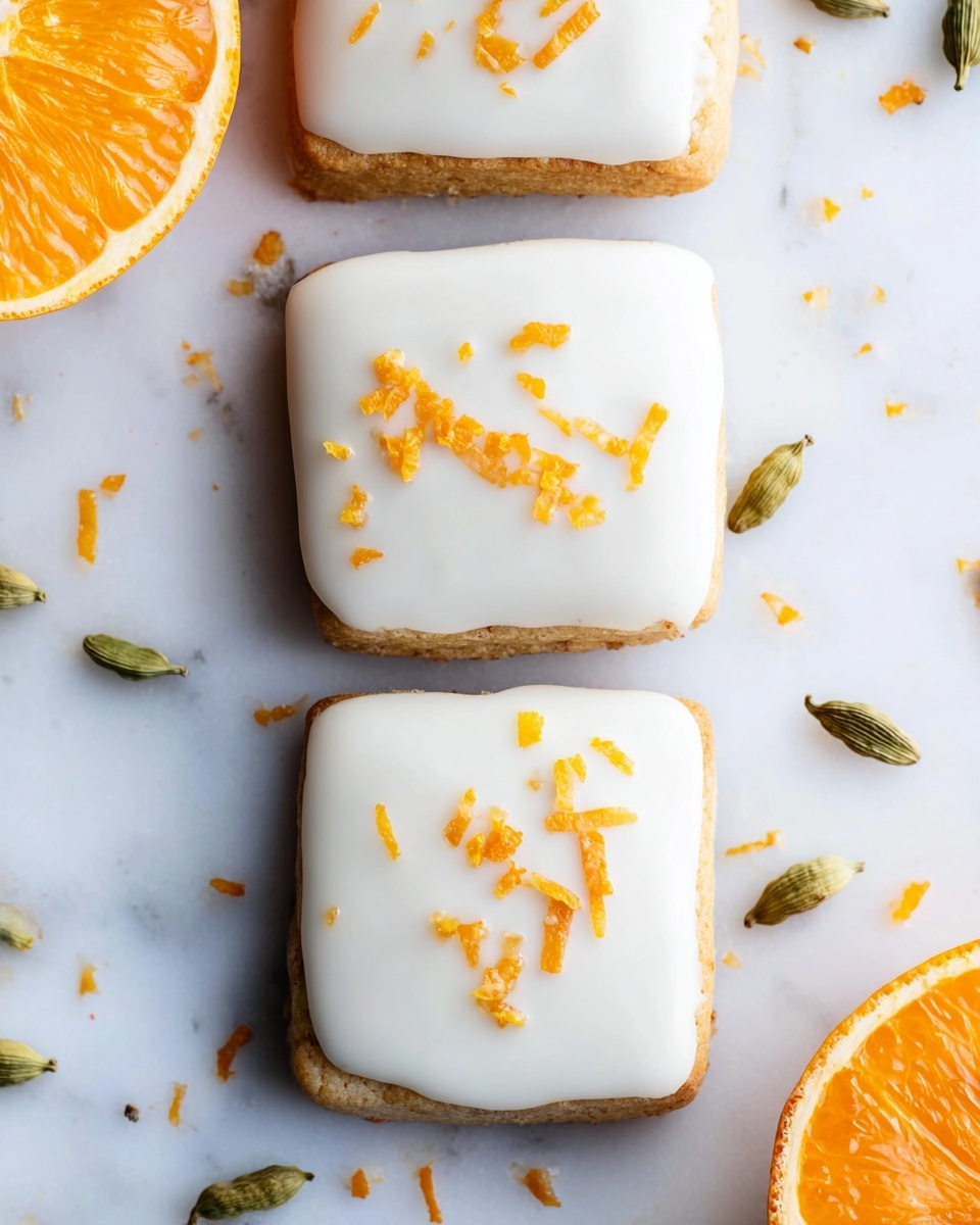 The image shows three square-shaped cookies arranged in a vertical line on a white marbled surface. Each cookie has a thick, smooth layer of white icing on top, sprinkled with small pieces of bright orange zest that add contrast and texture. The cookies themselves have light golden-brown edges visible under the icing. Scattered around the cookies on the white marbled surface are green cardamom pods and loose orange zest bits, adding a natural touch. On the left side, part of a fresh orange cut in half is visible, showing its bright, juicy orange flesh. The photo taken with an iphone --ar 4:5 --v 7