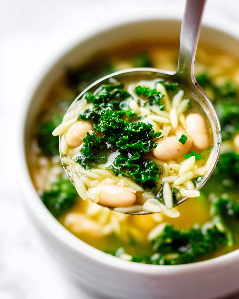A close-up view of a metal ladle holding soup above a white bowl filled with more of the same soup, resting on a white marbled surface. The soup has three main layers: the top layer is bright green kale leaves with a curled texture, the middle layer shows creamy white beans with a smooth surface, and the bottom layer contains light yellow pasta pieces that are thin and softly textured, all in a clear golden broth that shines with slight reflections. photo taken with an iphone --ar 4:5 --v 7