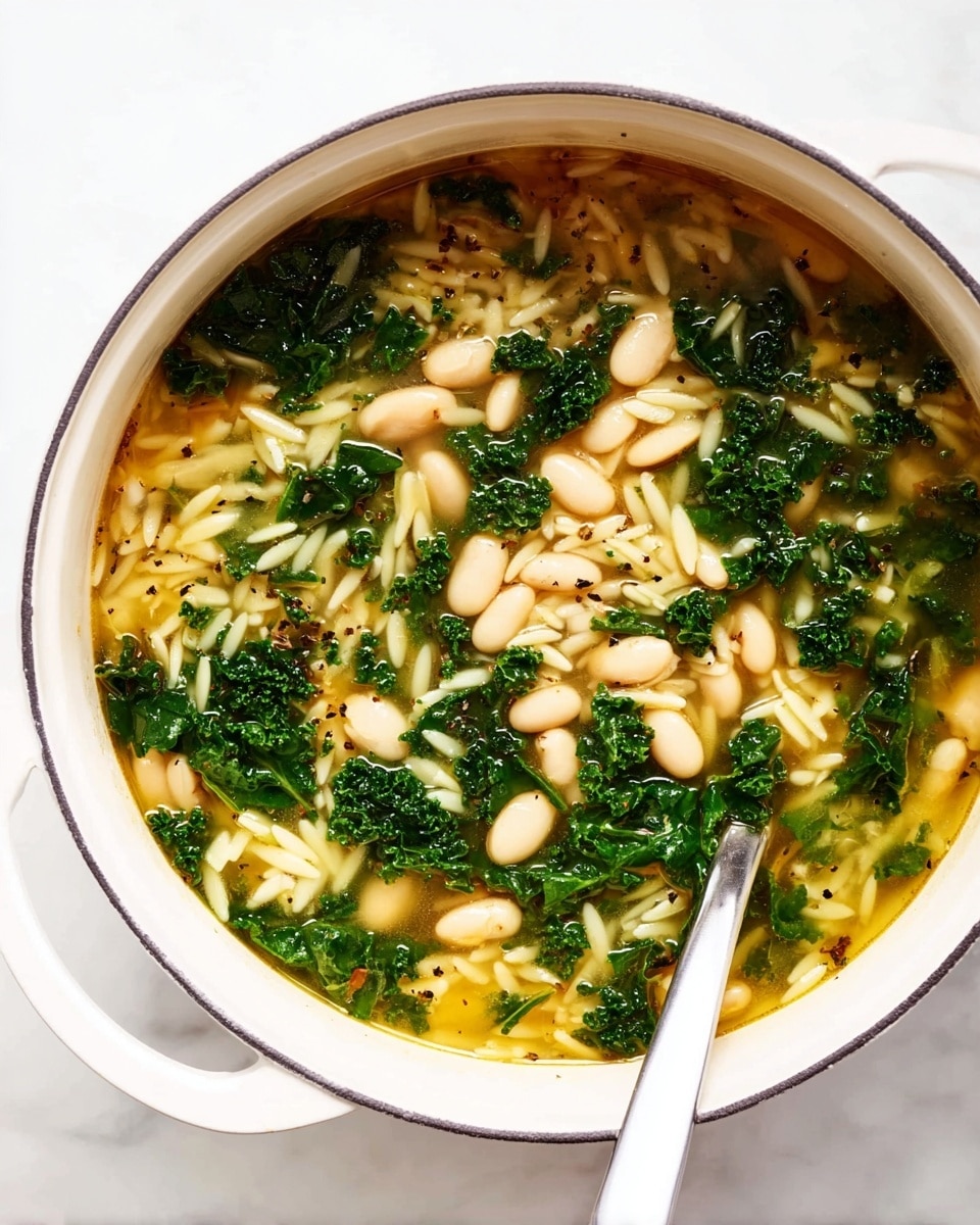 A white pot filled with soup showing three main layers: a light golden clear broth base, a middle layer of small white beans scattered evenly, and a top layer of bright green kale pieces mixed throughout with thin, white orzo pasta. Black pepper specks dot the surface. A silver spoon is resting inside the pot. The pot is placed on a white marbled surface photo taken with an iphone --ar 4:5 --v 7