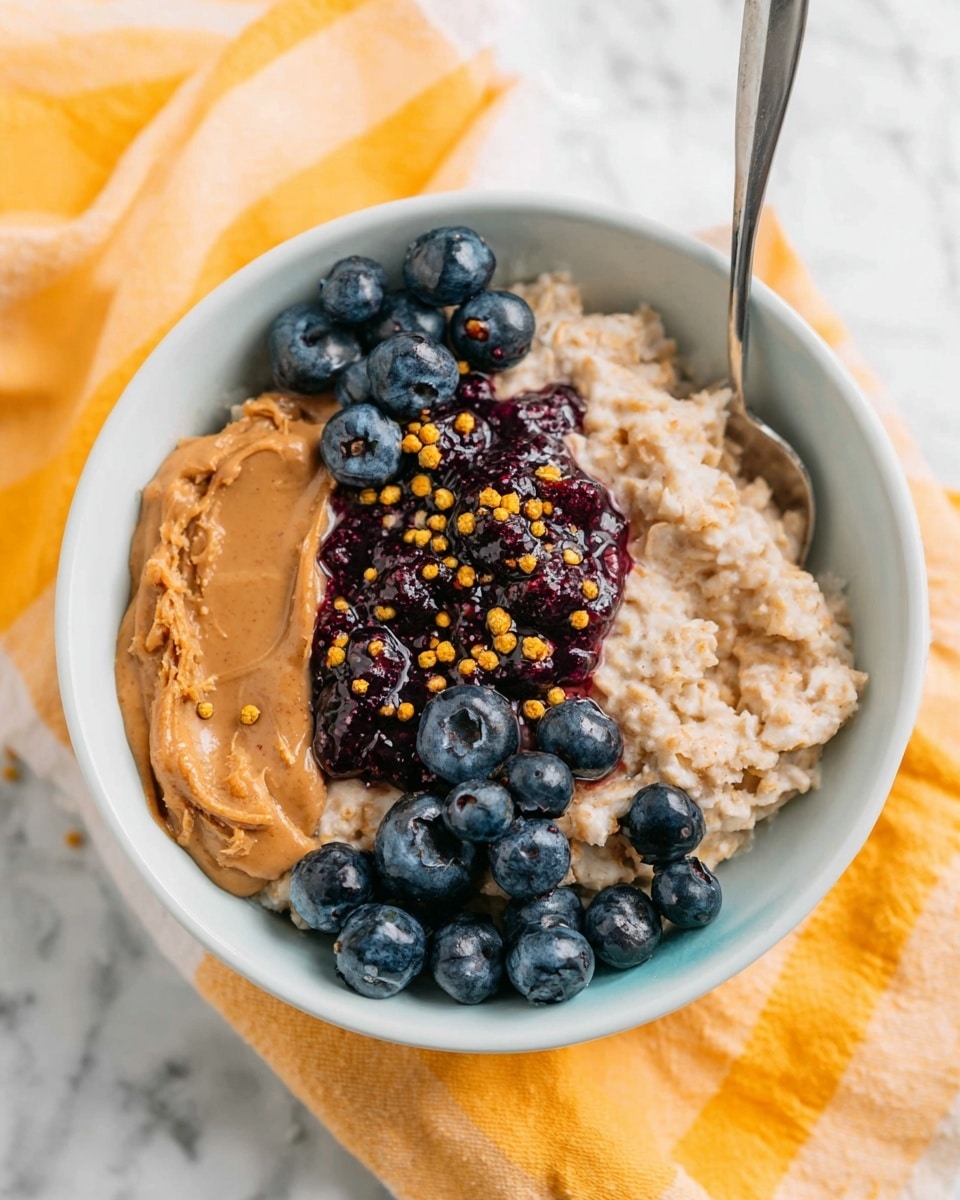 A white bowl filled with creamy oatmeal forms the base layer, topped with a layer of smooth, light brown peanut butter spread across one side. Next to this is a dollop of dark purple jam, slightly shiny and thick, placed between the peanut butter and fresh blueberries. The blueberries are scattered on one side, round and deep blue with a slight shine. On top of the peanut butter, there are scattered small yellow bee pollen granules adding texture. A metal spoon rests inside the bowl with its handle extending out. The bowl sits on a soft white and yellow cloth, all placed on a white marbled surface. Photo taken with an iphone --ar 4:5 --v 7