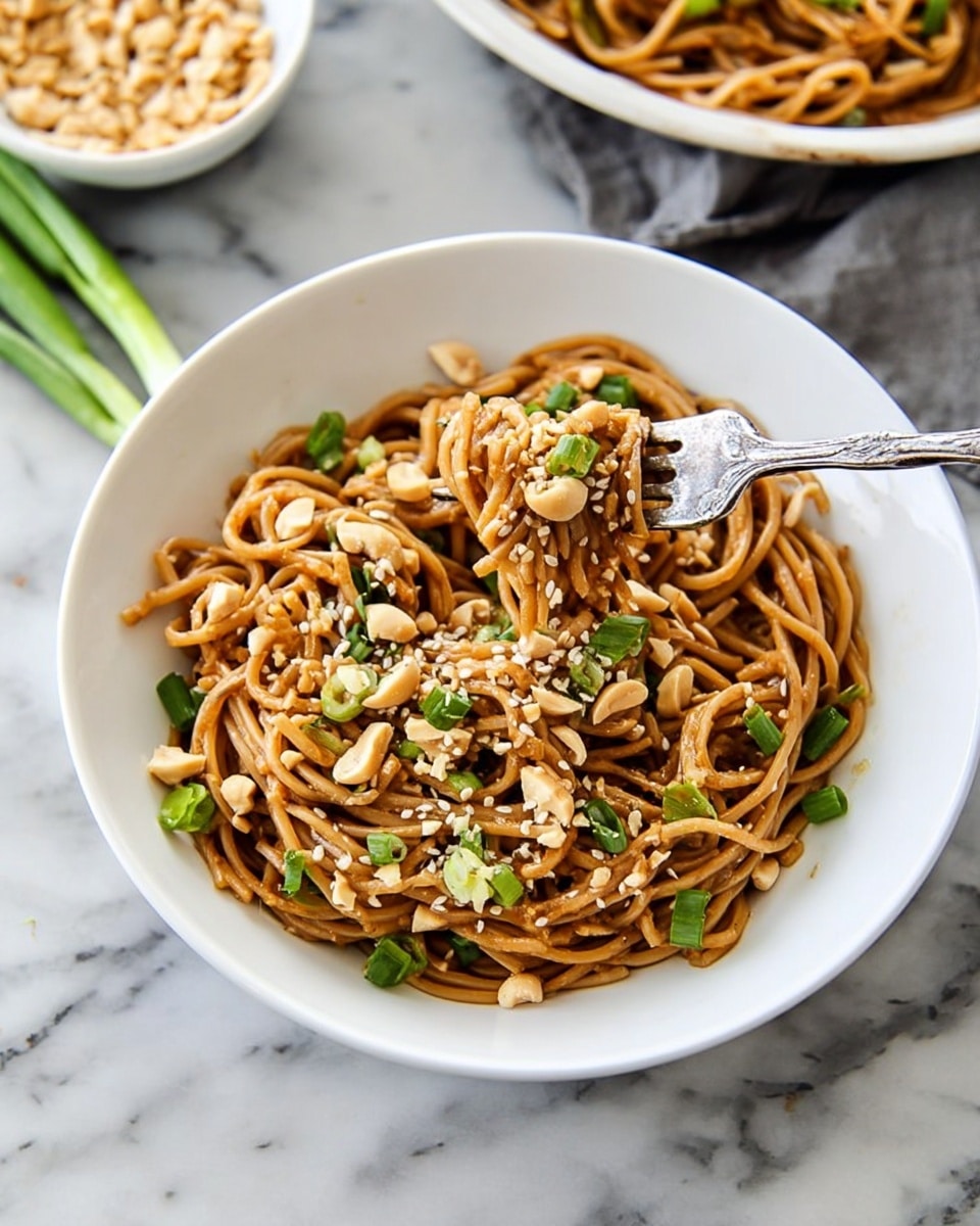 A white bowl filled with a single layer of brown noodles mixed with chopped green onions and scattered peanuts, topped with small white sesame seeds. A silver fork is twisted into some noodles near the center of the bowl, lifting them up. The bowl is placed on a white marbled surface with a green onion trimmed and lying nearby. In the background, there’s a partial view of another white bowl with more noodles and a small white bowl filled with sesame seeds. Photo taken with an iphone --ar 4:5 --v 7