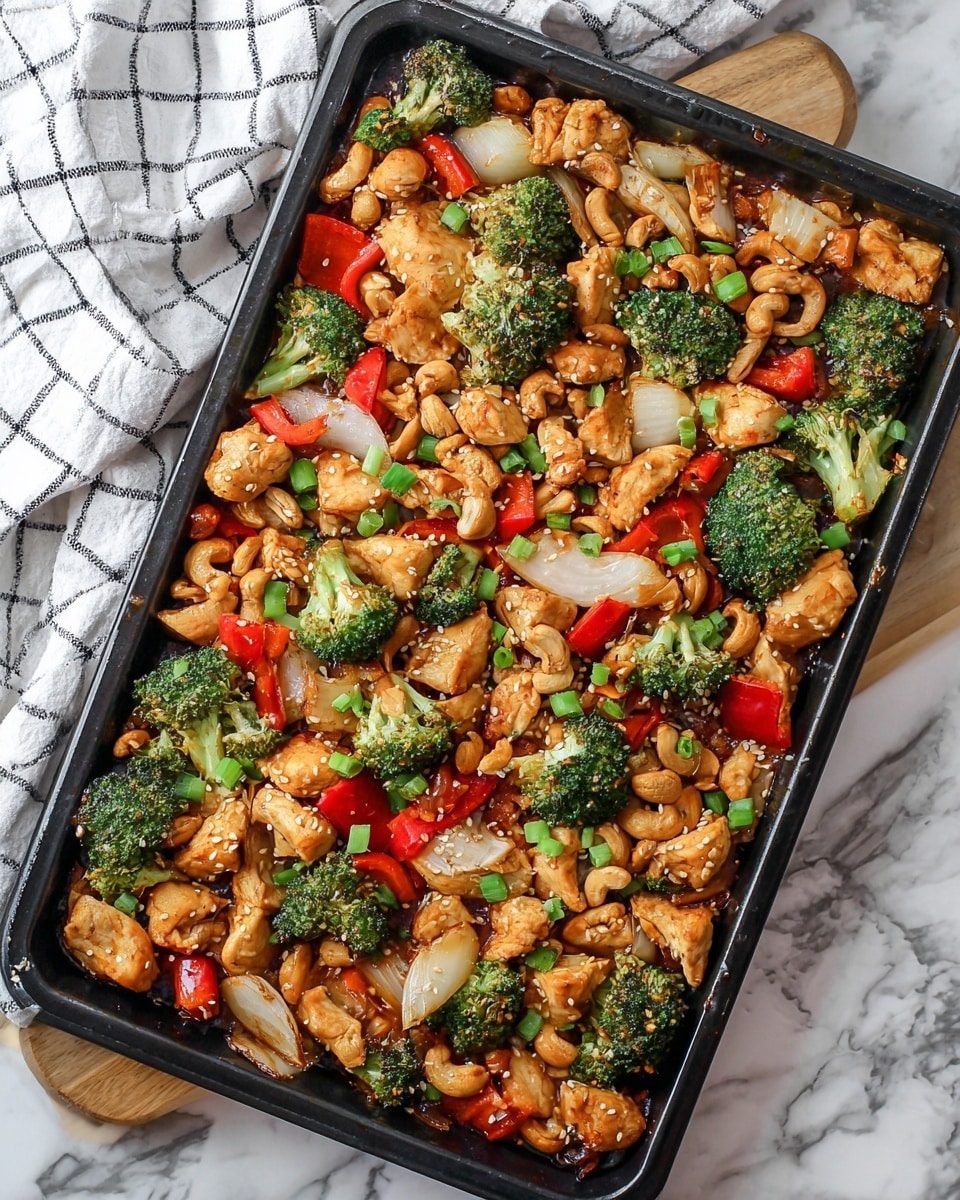 The image shows a large black baking tray filled with a colorful stir-fry dish that has three main layers: chunks of light golden cooked chicken scattered all over, bright green broccoli florets spread evenly, and large pieces of translucent white onion mixed with bright red bell pepper pieces. The dish is garnished with light brown cashew nuts, green chopped spring onions, and sprinkled white sesame seeds. The baking tray is placed on a white marbled surface with a white and black checkered cloth visible on one side. Photo taken with an iphone --ar 4:5 --v 7
