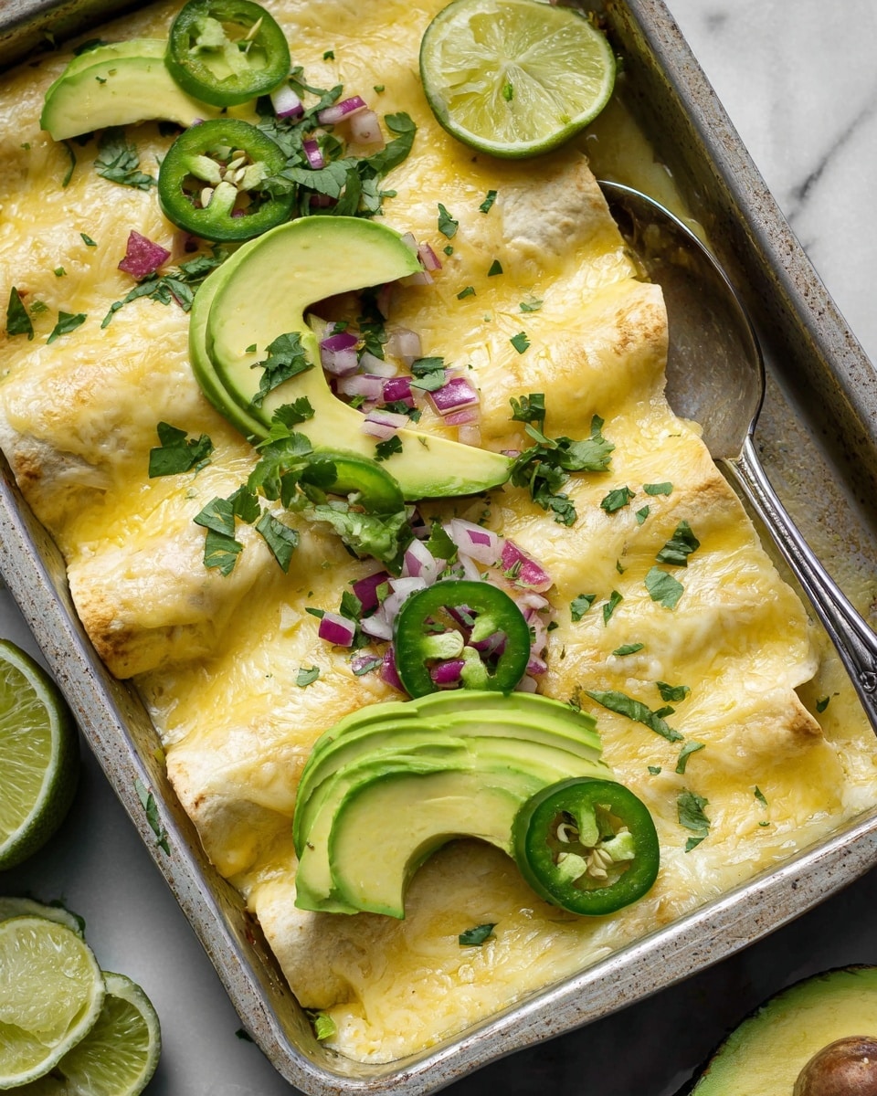 The image shows a metal baking dish filled with five rolled tortillas covered in melted light yellow cheese, giving a smooth and slightly golden texture. On top, there are thin green slices of avocado laid in pairs over the tortillas. Slices of fresh lime with a bright green rind and light green inside are placed on the cheese. Small pieces of red onion and chopped cilantro are scattered over the dish, adding pops of purple and green. Round green jalapeño slices with seeds visible are also placed on top. The dish is set on a white marbled surface, and a silver serving spoon rests in the corner of the dish. Photo taken with an iphone --ar 4:5 --v 7