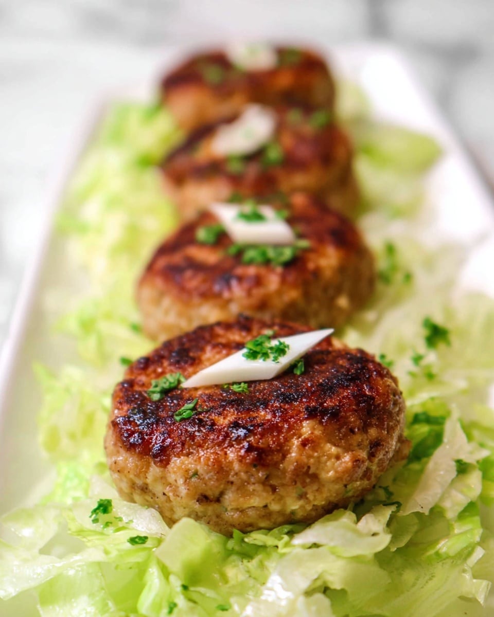 The image shows a row of four round, golden-brown patties with a slightly crispy texture on top, placed in a straight line on a bed of shredded light green lettuce. Each patty is topped with a small white triangular piece and sprinkled with small green herbs, giving a fresh touch. The lettuce underneath looks fresh and bright, filling the white plate that rests on a white marbled surface. The focus is on the closest patty, with the other patties gradually blurred in the background. photo taken with an iphone --ar 4:5 --v 7