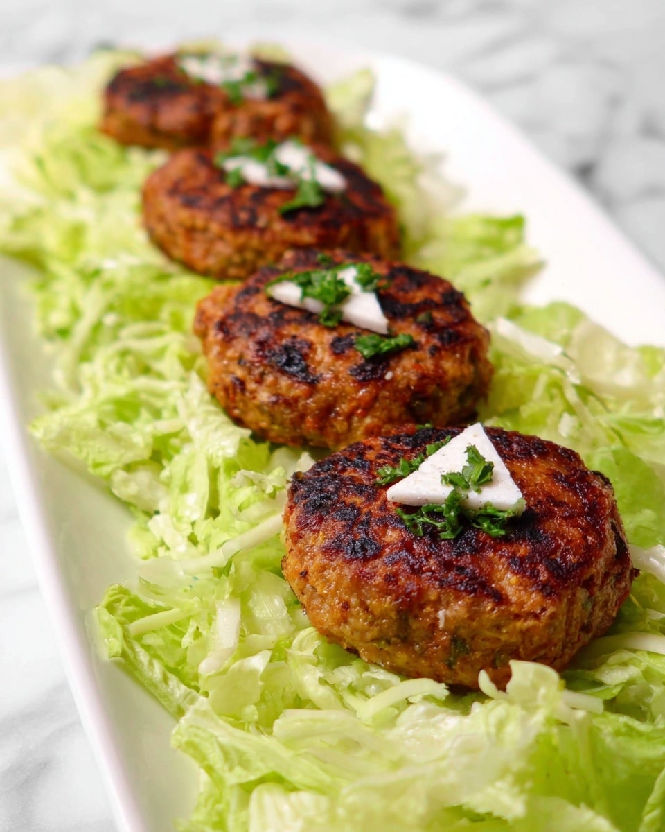 The dish shows a row of four round patties with a golden-brown, slightly charred texture on top of a bed of light green shredded lettuce. Each patty is decorated with a small white triangular piece and sprinkled with chopped green herbs. The patties are placed in a straight line in the center of a white plate, with the lettuce spread evenly around them. The background has a white marbled texture. photo taken with an iphone --ar 4:5 --v 7