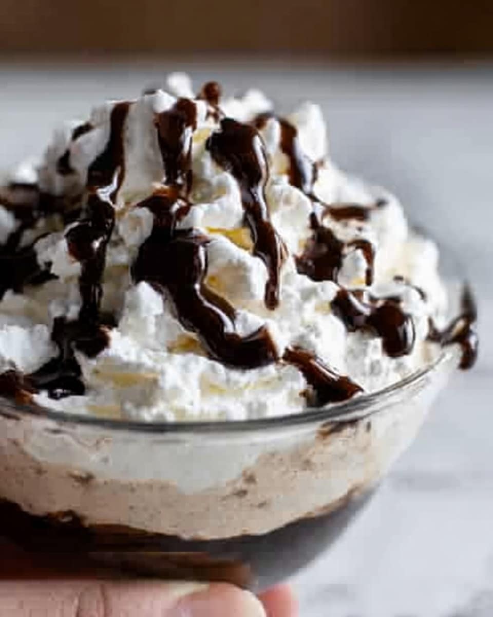 The image shows a close-up of a dessert with three clear layers in a white bowl on a white marbled surface. The bottom layer is light brown and creamy, the middle layer is thick white whipped cream with soft, fluffy texture, and the top layer is a dark, shiny chocolate sauce drizzled unevenly over the whipped cream. A woman's hand is holding the bowl slightly from one side. photo taken with an iphone --ar 4:5 --v 7