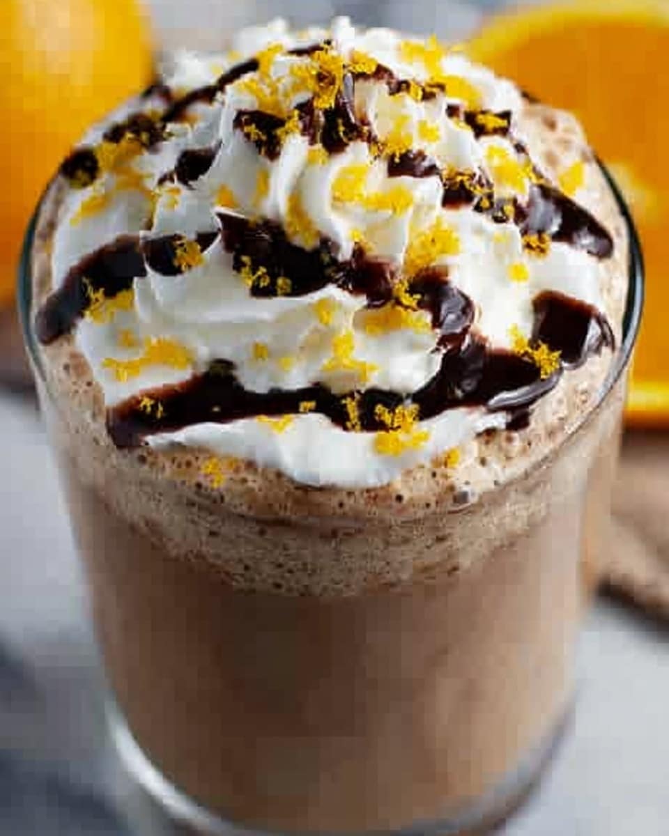 The image shows a close-up of a glass filled with a light brown creamy drink, topped with a large swirl of white whipped cream in the center. Over the whipped cream, there is a drizzle of dark brown chocolate sauce in loose patterns. Small yellow-orange crumbs or zest pieces are sprinkled evenly over the whipped cream and chocolate sauce, adding bright color contrasts. The glass sits on a white marbled surface with a blurry yellow object in the background. Photo taken with an iphone --ar 4:5 --v 7