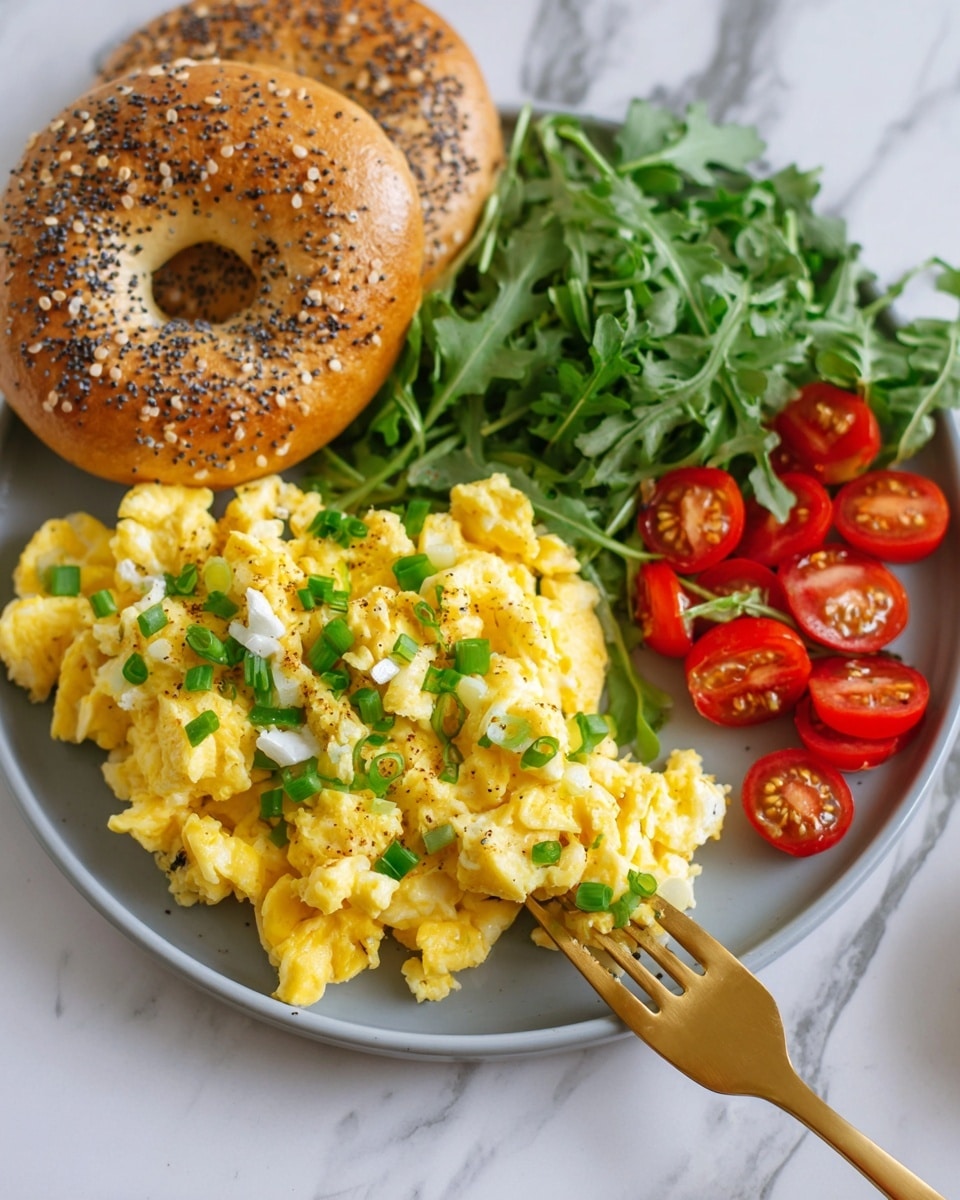 A white plate holds three main parts: on the left is a golden brown bagel with sesame and poppy seeds on top, with a shiny crust and soft texture. In the front center, there is a pile of fluffy yellow scrambled eggs mixed with small white pieces of egg white and topped with chopped green onions, giving a fresh touch. On the right side of the plate, there is a small salad with dark green arugula leaves and bright red cherry tomatoes, some whole and some sliced in half, showing their juicy inside. A gold fork touches the eggs, and the background is a white marbled texture. Photo taken with an iphone --ar 4:5 --v 7
