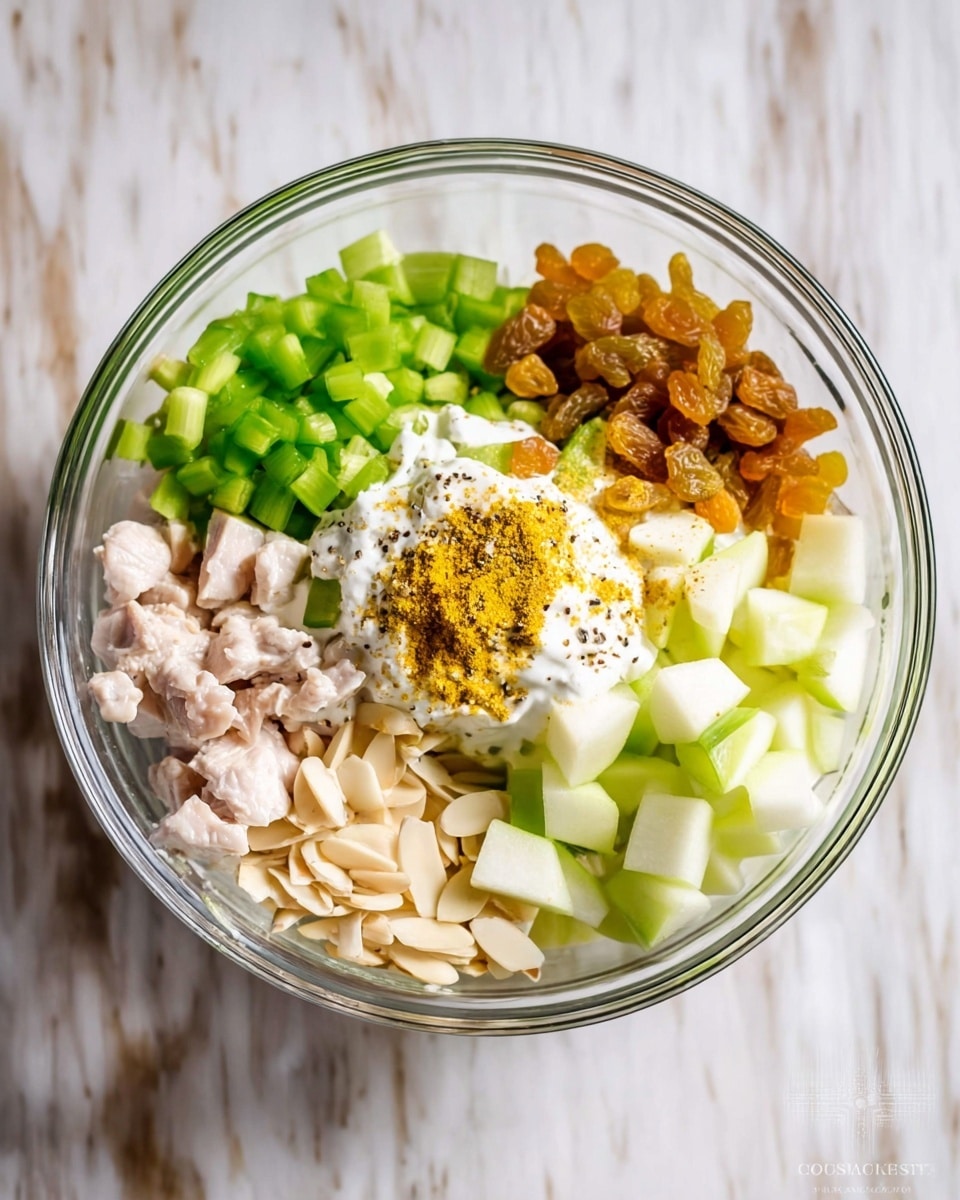 A clear glass bowl sits on a white marbled surface, filled with layers of fresh ingredients. Starting from the bottom left and going clockwise, there are small pieces of pale pink cooked chicken, golden raisins, bright green chopped celery, and light green and pale yellow diced apple. Near the bottom left are light beige slivered almonds, and above them some chopped green onions. In the center sits a dollop of creamy white yogurt topped with a sprinkle of yellow curry powder and black pepper. The colors are fresh, with contrasting textures of soft, crunchy, and smooth ingredients photo taken with an iphone --ar 4:5 --v 7