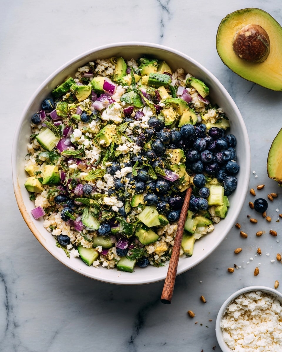 A white bowl filled with a colorful salad made of many small layers: the base is light-colored grains or small pieces, mixed with bright green chunks of avocado and cucumber, purple bits of onion, dark blue blueberries, and green herbs scattered throughout. On the side, a wooden spoon is partially inside the bowl. The bowl sits on a white marbled surface, and part of a halved avocado is visible at the top right. Some small scattered seeds or nuts, and a small white bowl with a white crumbly topping, are visible outside the bowl. photo taken with an iphone --ar 4:5 --v 7