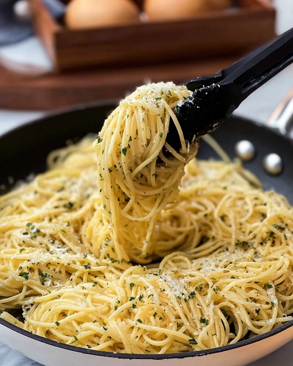 A close-up image of a large round white pan filled with spaghetti coated in a light yellow sauce. The pasta strands look soft and slightly shiny, sprinkled evenly with small green herb flakes and grated white cheese bits. A black pasta fork is lifting a twisted bundle of spaghetti from the center of the pan, showing the smooth texture of the noodles. The background is blurred but hints at a white marbled surface and a brown basket with some round objects. photo taken with an iphone --ar 4:5 --v 7