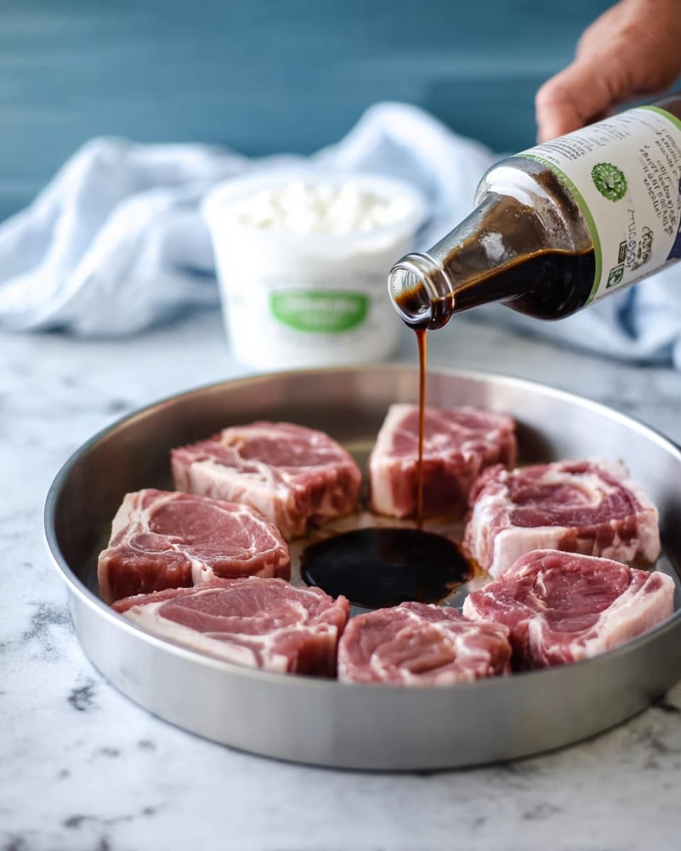 A round silver pan contains six pieces of raw meat arranged in a circle with a small space in the center. The meat is pink with white edges of fat. A dark brown sauce is being poured from a clear glass bottle by a woman's hand into the center space of the pan, forming a small pool. In the background, there is a white container of Greek yogurt on a blue surface, with a light-colored cloth blurred behind it. The overall setting is on a white marbled textured surface. photo taken with an iphone --ar 4:5 --v 7