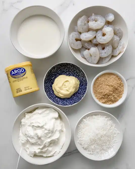 The image shows six items on a white marbled surface. At the top right, there is a white bowl filled with raw shrimp, pale gray with some translucent parts, arranged loosely. To the left of it, there is a white bowl filled with smooth, off-white coconut milk. Below the shrimp bowl, there is a white bowl filled with thick, whipped coconut cream, which is bright white with a slightly fluffy texture. In the middle, a small white bowl with a dark blue pattern holds a dollop of light yellow mayo, smooth and creamy. To the right, a small white bowl contains light brown crumbly coconut sugar. Next to it at the bottom right, a small plain white bowl is filled with shredded coconut, white and flaky in texture. Finally, a yellow container of ARGO corn starch stands upright on the surface. photo taken with an iphone --ar 4:5 --v 7