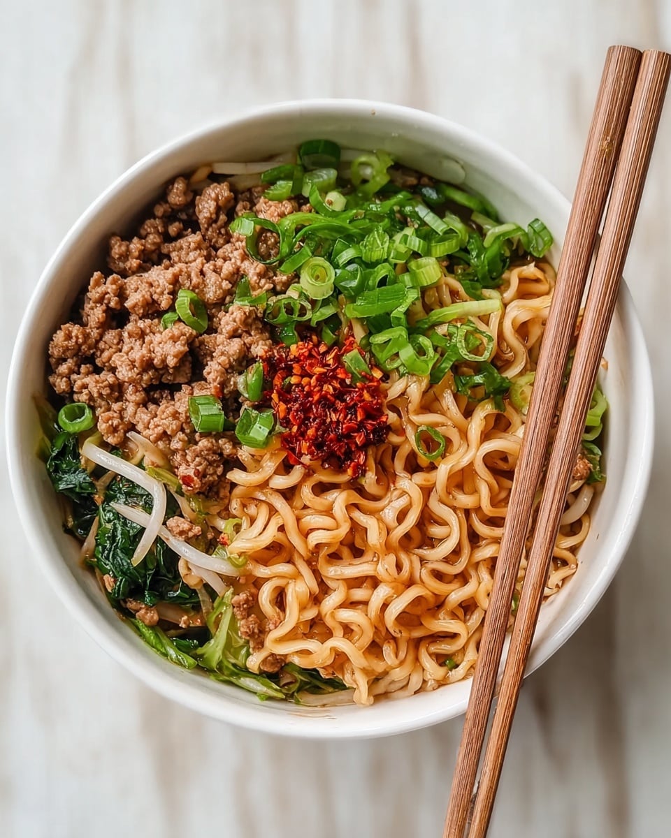 A white bowl filled with three layers of food: the bottom layer is curly light brown noodles with a shiny, slightly oily texture; the middle layer consists of small pieces of cooked ground meat mixed with green leafy vegetables and white bean sprouts; the top layer has bright green chopped spring onions and a small mound of red chili flakes on one side. A pair of wooden chopsticks rests diagonally on the edge of the bowl against a white marbled surface. photo taken with an iphone --ar 4:5 --v 7