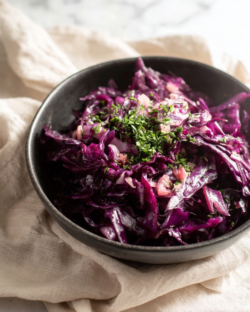 A black bowl filled with a single layer of finely sliced deep purple cabbage mixed with small bits of pinkish-red and white ingredients, topped with a light sprinkle of bright green chopped herbs. The cabbage looks fresh and slightly shiny, suggesting a light dressing. The bowl is placed on soft, light beige cloth with folds. The background has a white marbled texture. Photo taken with an iphone --ar 4:5 --v 7