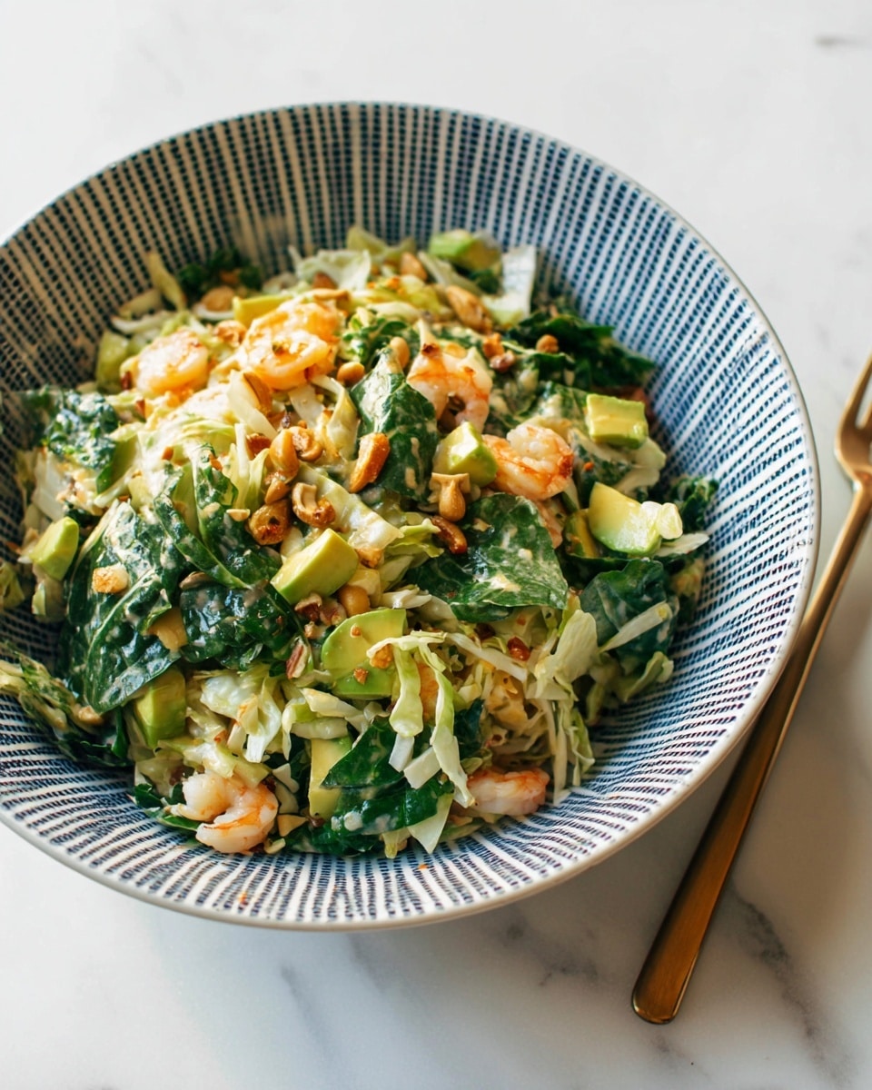 A white bowl with a blue grid pattern is filled with a mixed salad that has three main layers: large green leafy pieces on the top and throughout, light yellow or white shredded pieces mixed in and golden brown roasted nuts spread evenly. Inside the salad, there are chunks of yellow-green avocado and small shrimp pieces with an orange tint, all combined with a light dressing that gives the dish a fresh and colorful look. The bowl is placed on a white marbled surface, and to the side, there is a bronze-colored fork. photo taken with an iphone --ar 4:5 --v 7