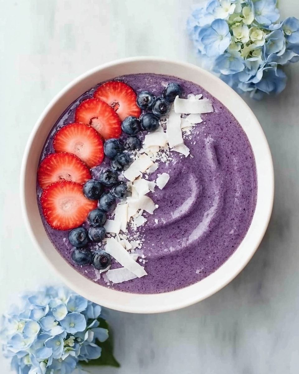 A white bowl filled with a thick, smooth purple smoothie takes up most of the image, with the smoothie swirling gently. On the left edge of the smoothie, there are fresh red strawberry slices, round dark blue blueberries, and white shredded coconut pieces neatly arranged in lines. The bowl sits on a white marbled surface with light blue hydrangea flowers placed around it for decoration. Photo taken with an iphone --ar 4:5 --v 7