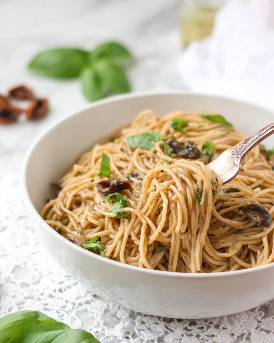 A white bowl filled with light brown spaghetti noodles mixed with small pieces of mushrooms and bits of sun-dried tomatoes, topped with bright green fresh basil leaves scattered on top and around. A silver fork is partially inserted into the noodles on the right side of the bowl. The bowl sits on a white lace cloth on a white marbled surface, with some whole sun-dried tomatoes placed nearby and a bunch of fresh basil leaves in the background. Photo taken with an iphone --ar 4:5 --v 7