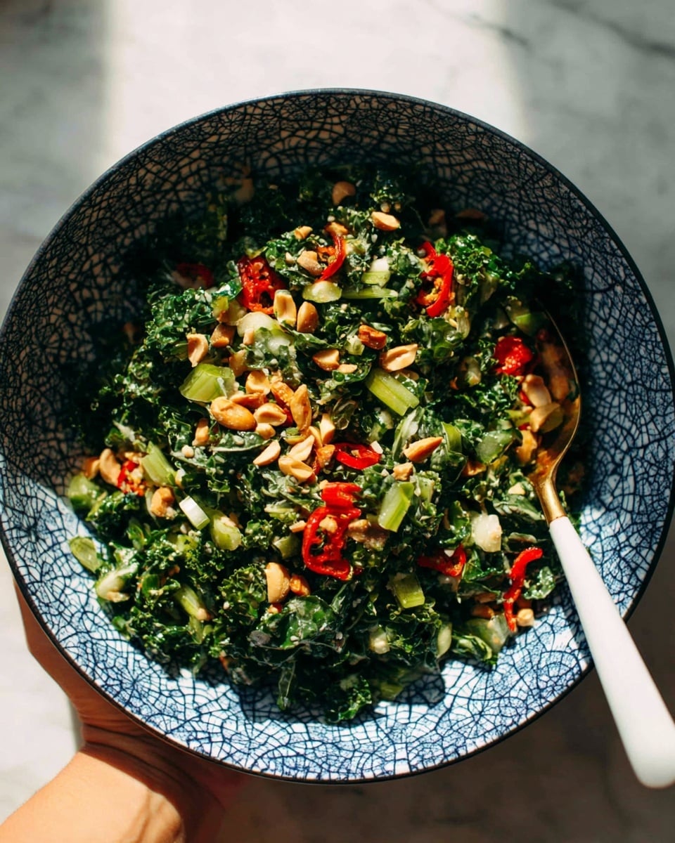 A large bowl with a blue and white cracked pattern holds a vibrant salad made of dark green leafy kale mixed with bright green chopped scallions, small white onion pieces, and sliced red chili peppers scattered throughout. The top is sprinkled with light brown chopped peanuts, adding a crunchy texture. A white and gold spoon gently rests inside the bowl, and a woman's hand holds the bowl against a white marbled surface in the background. The lighting creates a warm and fresh feel. photo taken with an iphone --ar 4:5 --v 7
