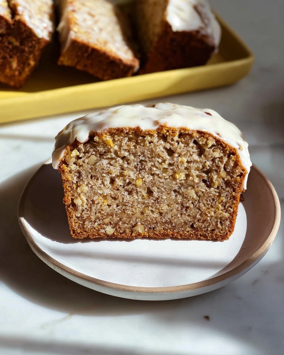 The image shows a loaf cake sliced into five pieces on a white rectangular plate. Each slice has a thick layer of smooth, creamy white frosting spread evenly on top, slightly dripping down the sides. The cake itself is a medium brown color with a slightly crumbly texture. In the background, there is a clear glass jar filled with a light brown creamy substance, and a small section of a yellow bowl is visible on the right side. The setting is on a white marbled surface with soft natural light creating gentle shadows. Photo taken with an iphone --ar 4:5 --v 7