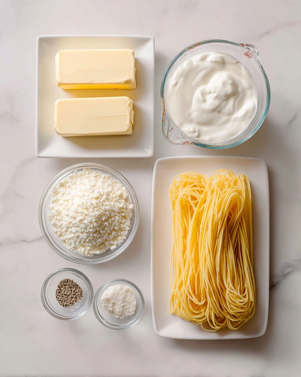 The image shows ingredients neatly arranged on a white marbled surface, ready for cooking. On the top left, there are two pale yellow sticks of butter on a white square plate. To the right of the butter, a clear measuring cup filled with white cream is placed. On the far right, a white rectangular plate holds long, uncooked yellow pasta strands stacked evenly. Below the butter, there are two small glass bowls with white powdery cheese, the one on the left is slightly finer and brighter, the other more off-white and granular. Below and slightly to the left, two tiny glass bowls hold salt mixed with black pepper and a light beige powder. All items are set with space between them, showing clean arrangement and soft natural lighting. Photo taken with an iphone --ar 4:5 --v 7