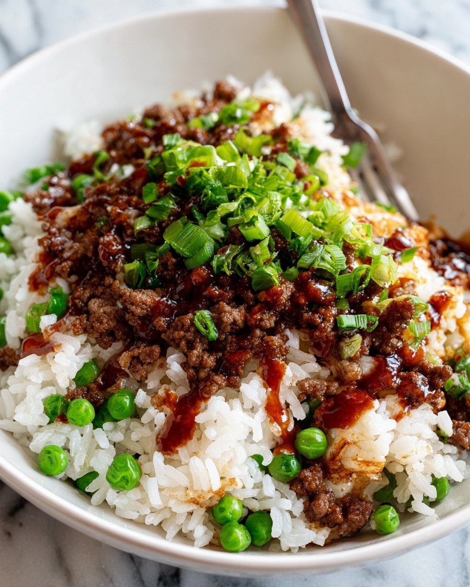 Two white ceramic bowls filled with fried rice are placed on a white marbled surface. Each bowl has a mix of light brown rice, darker brown cooked ground meat, and bright green peas scattered throughout. The fried rice is topped with fresh green sliced spring onions. A silver spoon rests inside the bowl in the foreground. To the right, there is a small black bowl filled with red chili sauce with chili flakes on top, and a dark spoon is dipped into it. A dark cloth is partly visible under the bowls. Photo taken with an iphone --ar 4:5 --v 7