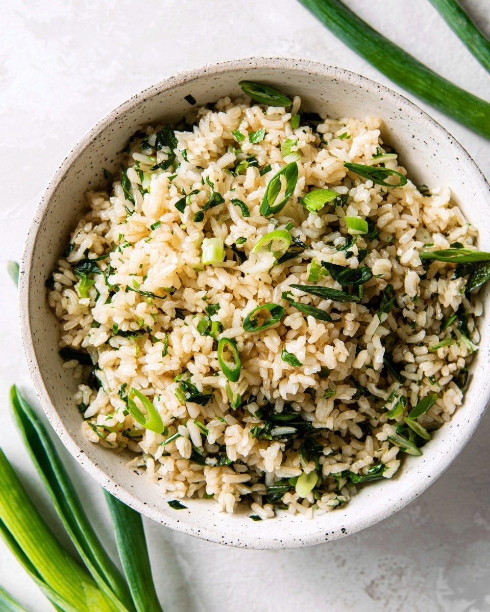 A large white bowl filled with cooked rice mixed with small green vegetable pieces and finely chopped green herbs evenly spread throughout. The rice is light brown with a slightly oily texture, and the green bits add a fresh look. The bowl sits on a white marbled surface with green okra pieces placed nearby, enhancing the natural and simple presentation. Photo taken with an iphone --ar 4:5 --v 7