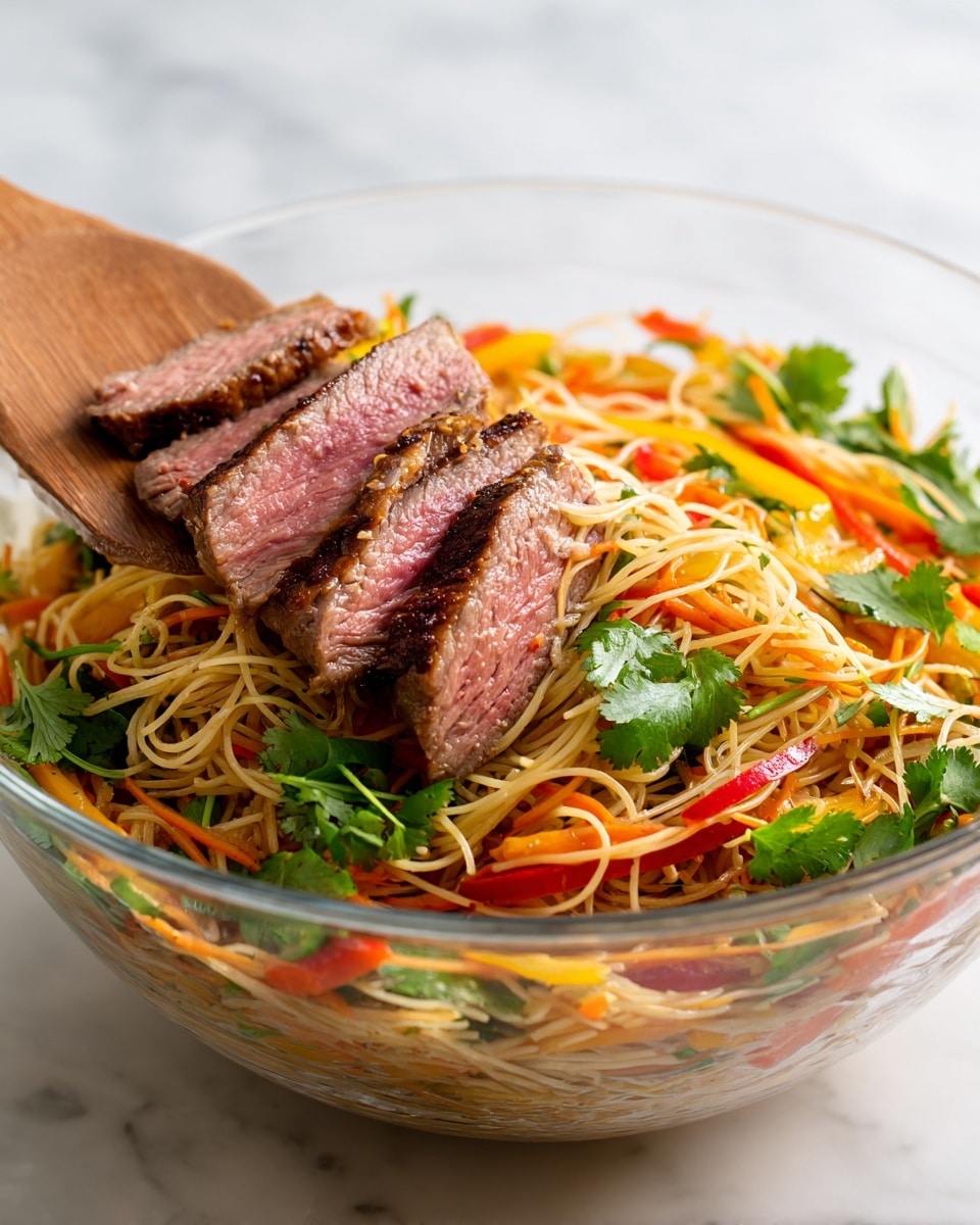 A clear glass bowl holds a colorful noodle salad with several layers. At the bottom, light brown noodles form a soft base. Mixed through the noodles are thin strips of bright orange carrots, red bell peppers, and yellow mango, adding vibrant colors. On top, there are medium pieces of grilled meat with a browned outside and pink inside. Fresh green cilantro leaves are scattered across the dish, adding texture and color. A wooden spatula is placed inside the bowl, lifting some of the salad. The bowl is set on a white marbled surface. Photo taken with an iphone --ar 4:5 --v 7