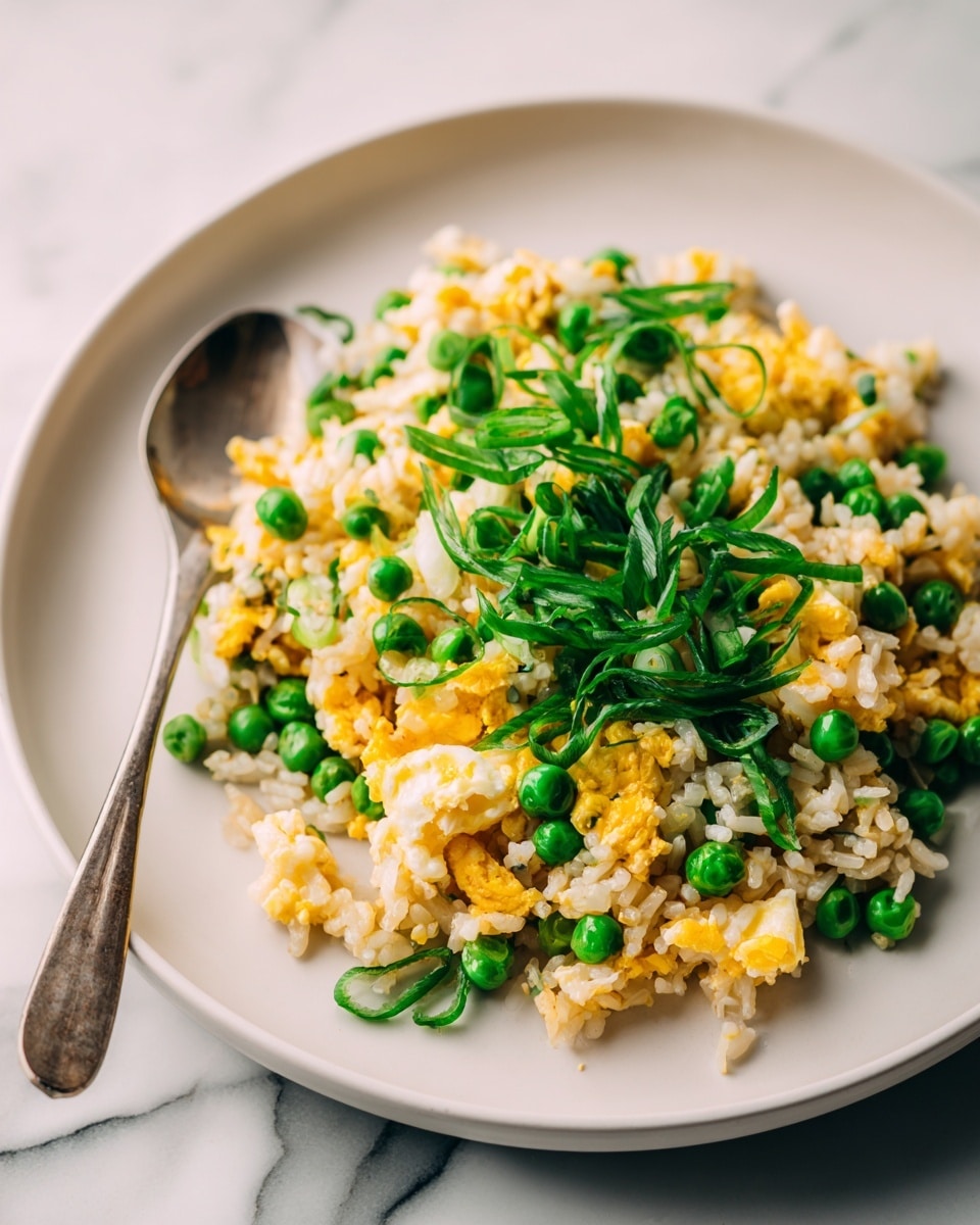 A close-up of a white plate with fried rice made of light brown cooked rice mixed with small bright green peas and scrambled yellow egg pieces. On top, fresh green scallion slices are scattered evenly. The plate is placed on a white marbled surface. photo taken with an iphone --ar 4:5 --v 7