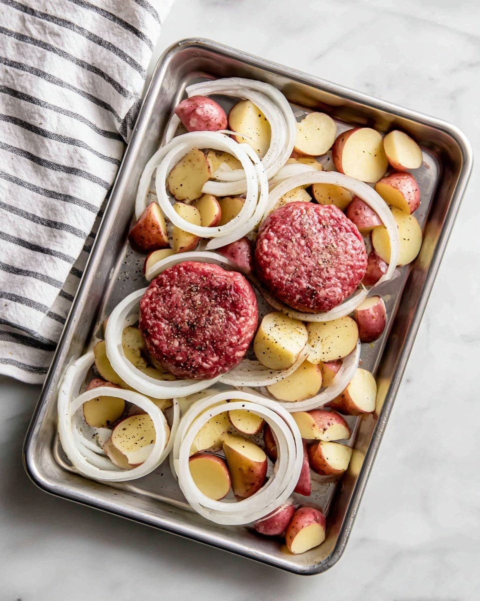 A silver baking tray on a white marbled surface holds two raw oval-shaped hamburger patties placed side by side near the center. Around the patties are many thin white onion rings spread evenly across the tray. Scattered among the onion rings, there are small chunks of red-skinned potatoes showing both their red outer skin and pale inner flesh. The entire tray has a light sprinkle of black pepper on top. A white towel with black stripes is partially visible on the left side of the tray. photo taken with an iphone --ar 4:5 --v 7