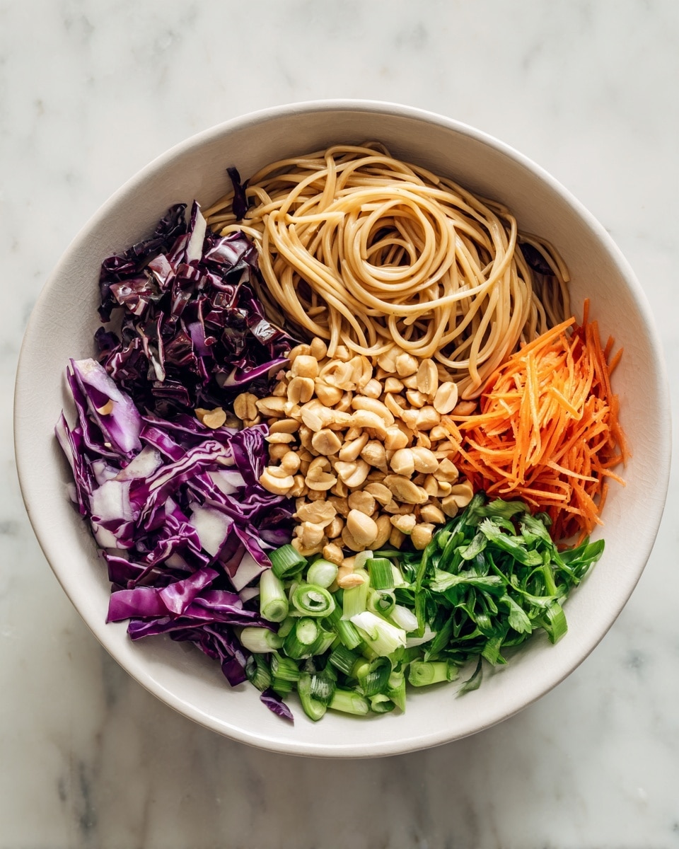 A white bowl on a white marbled surface holds five separate layers of ingredients arranged in sections. At the top right, there is a pile of light brown noodles with a smooth texture. To the left of the noodles, there are thin slices of dark purple cabbage with white veins. On the bottom right, bright green sliced scallions form a small section, next to a pile of fresh green chopped herbs. At the bottom center, there is a heap of coarsely chopped light brown peanuts. To the left of the peanuts, finely grated orange carrots add a bright splash of color. photo taken with an iphone --ar 4:5 --v 7