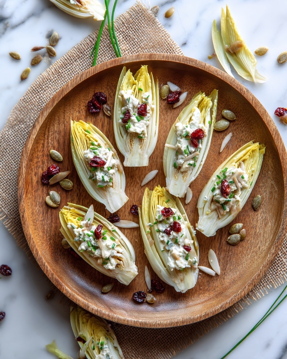 The image shows a round wooden tray with six light yellow endive leaves arranged neatly on it. Each leaf is topped with a creamy white salad that has small red pieces, likely dried cranberries, and some sprinkled green seeds. Around the tray on a white marbled textured surface are more endive leaves, scattered pumpkin seeds, dried cranberries, and green chives. The overall look is fresh, light, and inviting, with a natural rustic feel. photo taken with an iphone --ar 4:5 --v 7