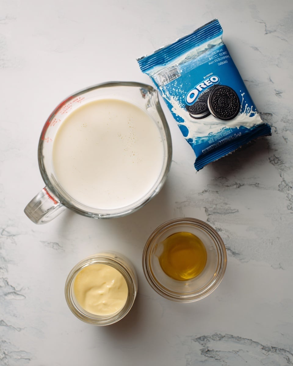 A clear glass measuring cup filled with white heavy cream sits on a white marbled surface, next to a blue package of Oreos with a splash of milk design on it. Below the measuring cup, there is a small clear glass jar with creamy yellow sweetened condensed milk inside, and near it is a small clear glass container holding golden vanilla extract. The items are spaced out on the white marbled background, showing simple baking ingredients. photo taken with an iphone --ar 4:5 --v 7