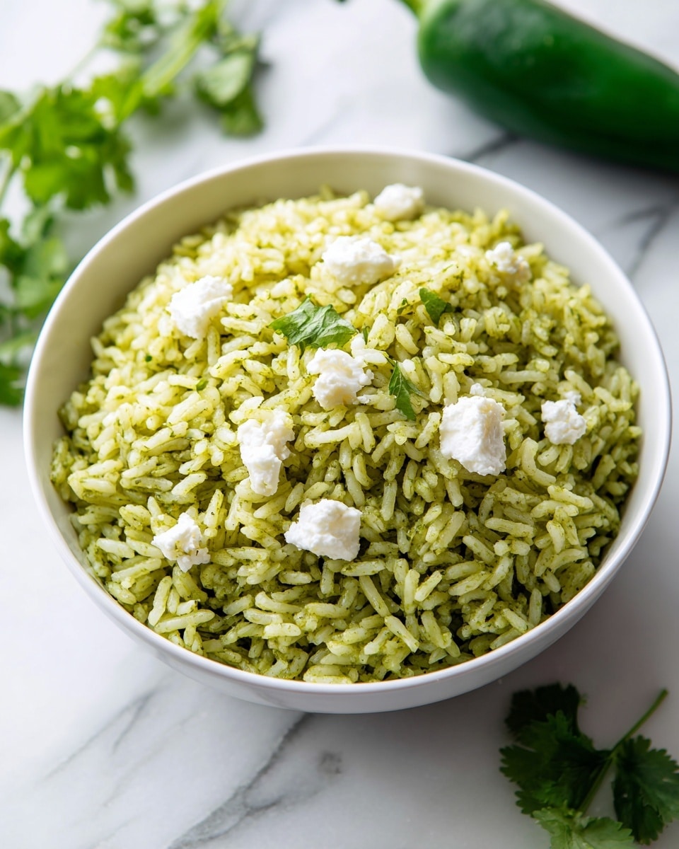 A white bowl filled with green rice that looks soft and fluffy, with each grain showing a mix of light and darker green shades. On top, there are scattered white cheese crumbles that add a rough texture and bright contrast. The bowl sits on a white marbled surface alongside fresh green cilantro leaves and a green bell pepper, giving a fresh and natural feel. The background is softly blurred to keep focus on the bowl. Photo taken with an iphone --ar 4:5 --v 7